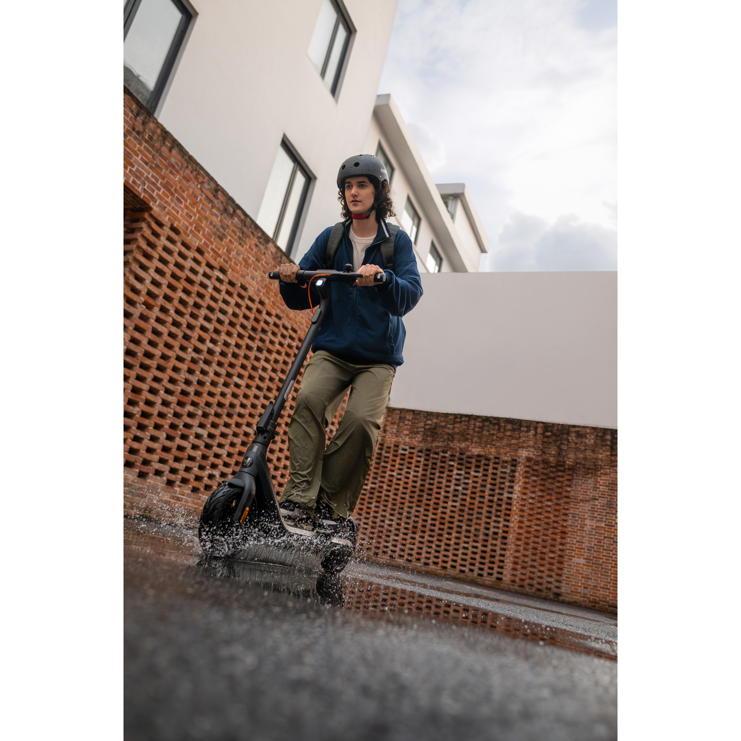 Personne faisant du scooter électrique sur une rue mouillée avec des bâtiments en arrière-plan.