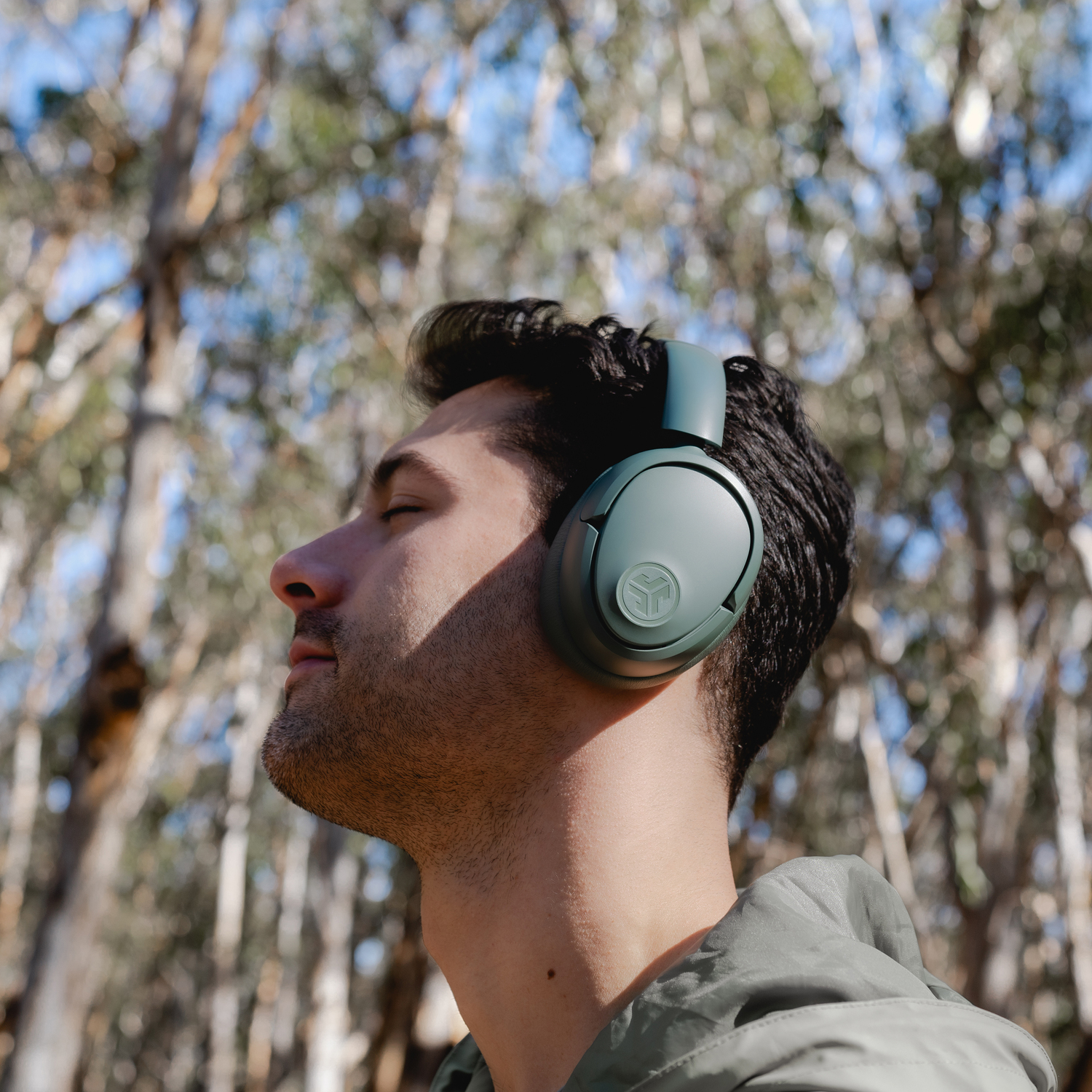 Man wearing dark green headphones, outside, trees in background.