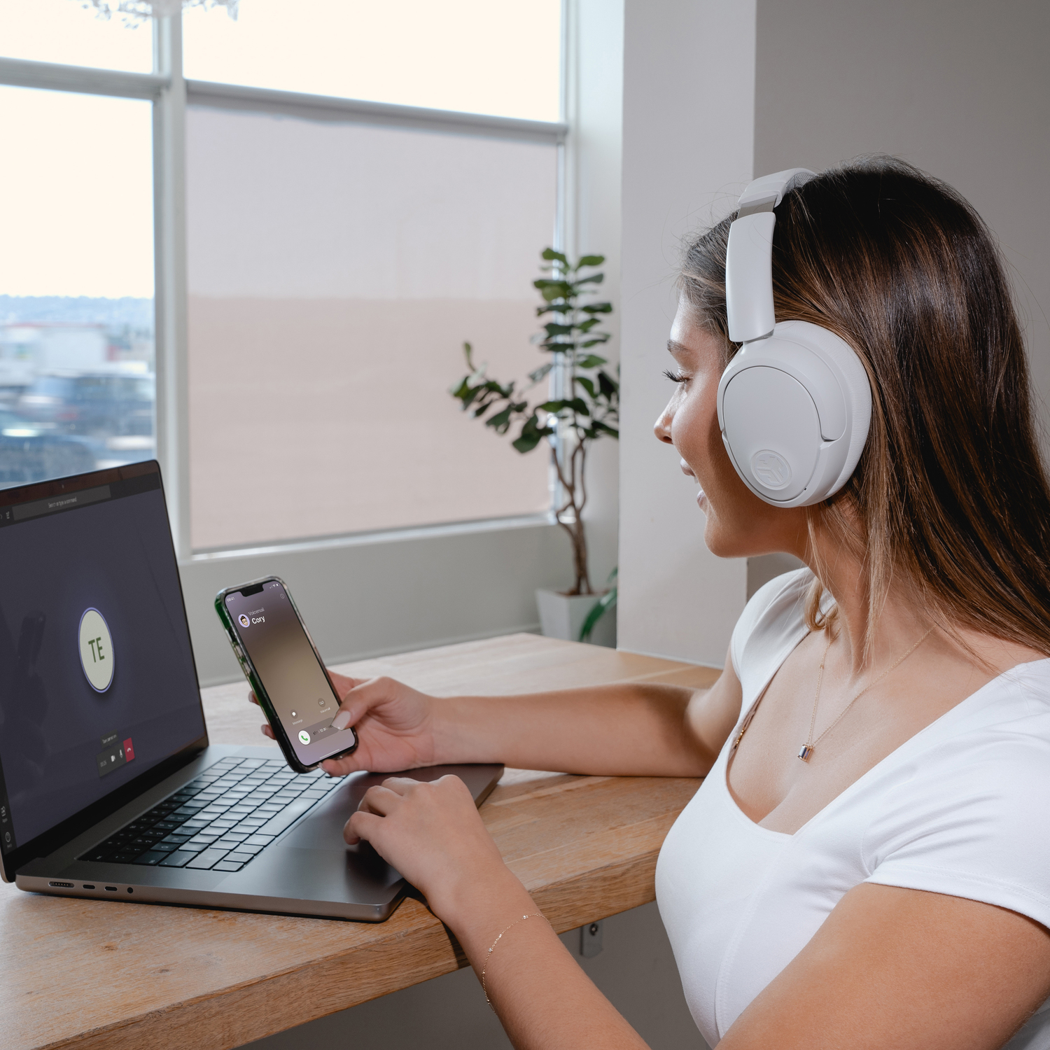 Vrouw die een laptop gebruikt, een koptelefoon draagt, een telefoon vasthoudt.
