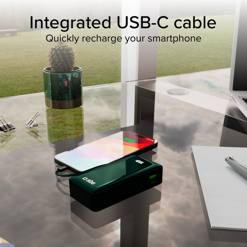 Szklany stół z ładującym się telefonem. Widoczny jest zielony power bank i materiały biurowe.