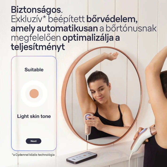 Nő szőrtelenítő készüléket használ, kerek tükörben. A pulton egy telefon látható.