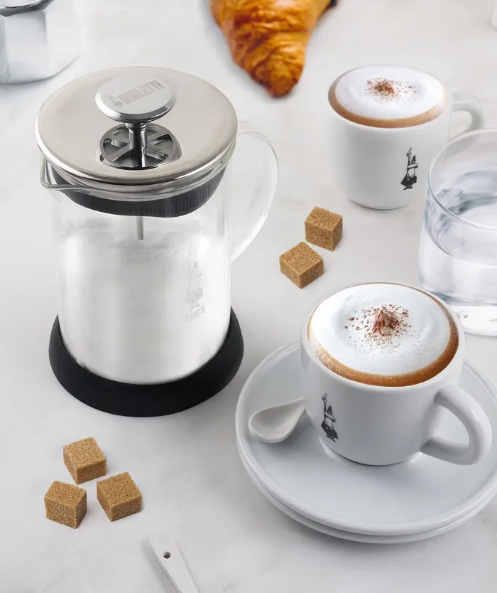 Asztal kávéval, kockacukorral és egy french press-szel. Két csésze cappuccino van a képen.
