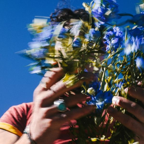Verschwommenes Bild einer Person, die einen Strauß blauer Blumen vor blauem Himmel hält.