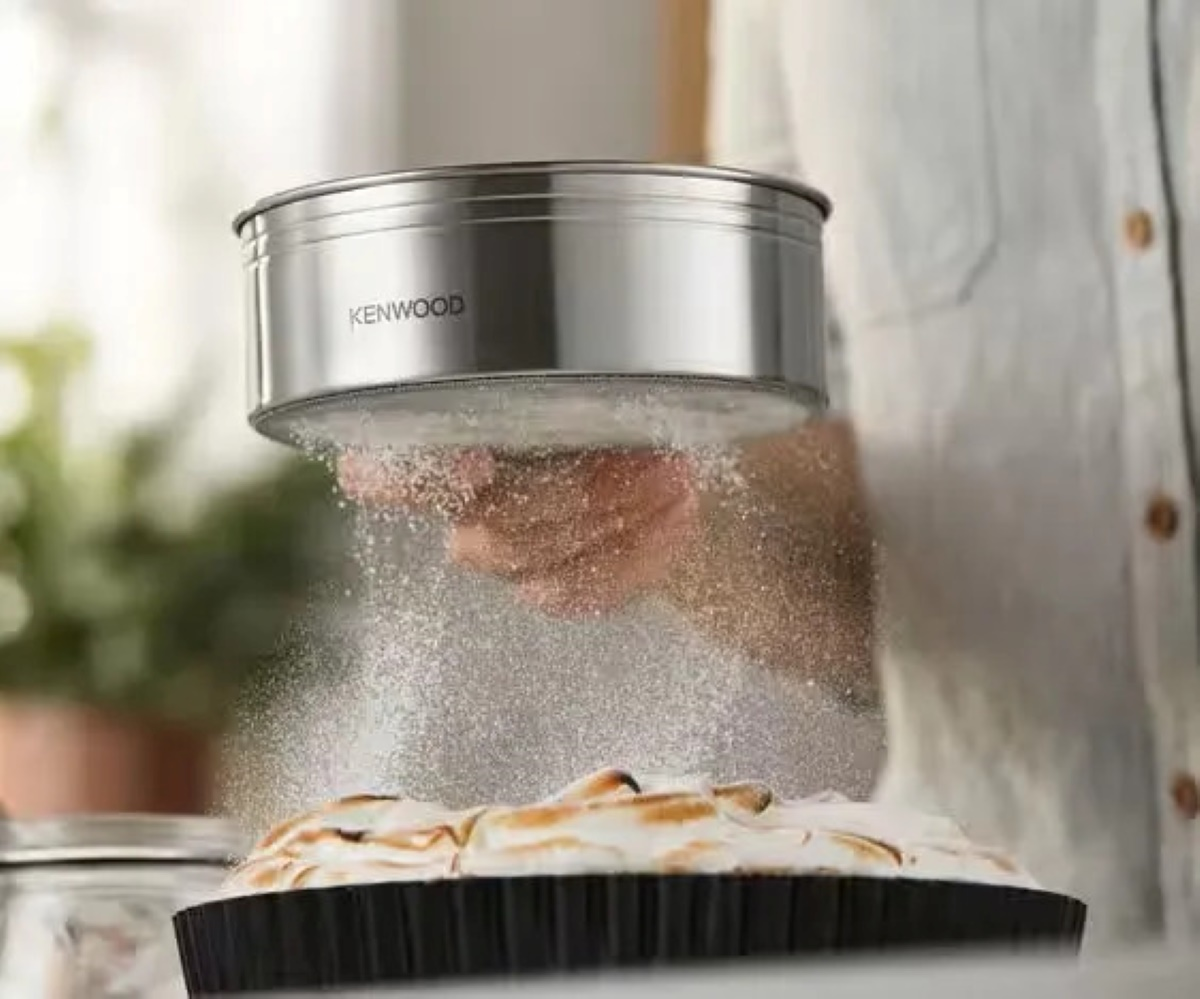Przesiewacz Kenwood posypuje ciasto cukrem pudrem. Ciasto jest w czarnej formie do tarty.