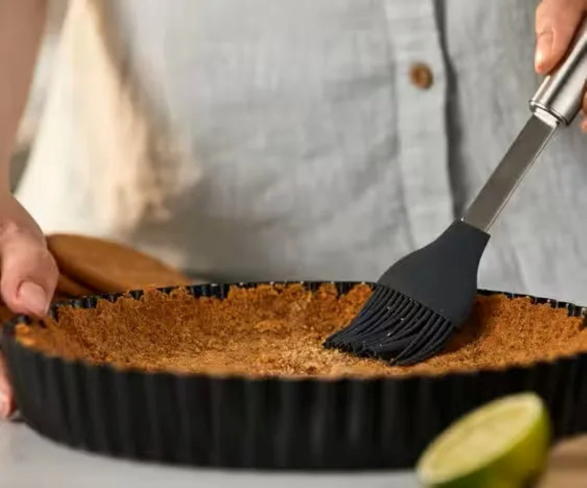 Osoba pędzlem smarująca spód ciasta. Limonka w tle.