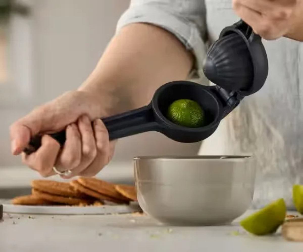 Osoba wyciskająca limonkę w czarnej wyciskarce nad beżową miską.