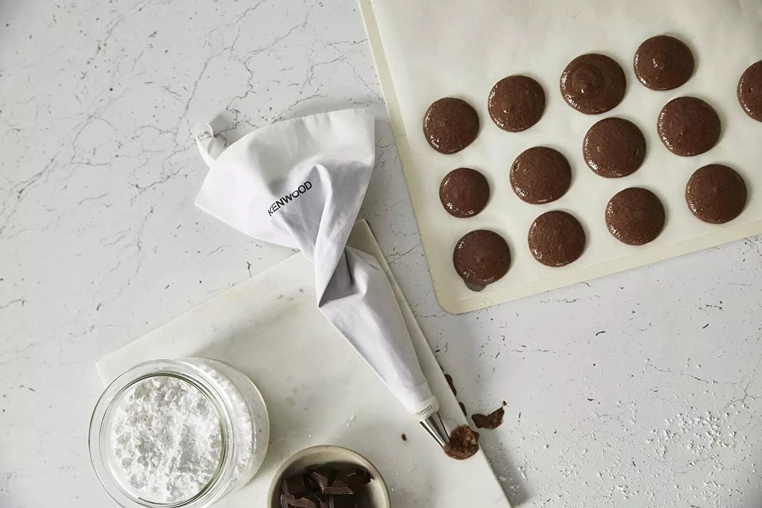 Rękaw cukierniczy, słoik z mąką i kawałki czekolady na marmurze z ciastem na makaroniki.