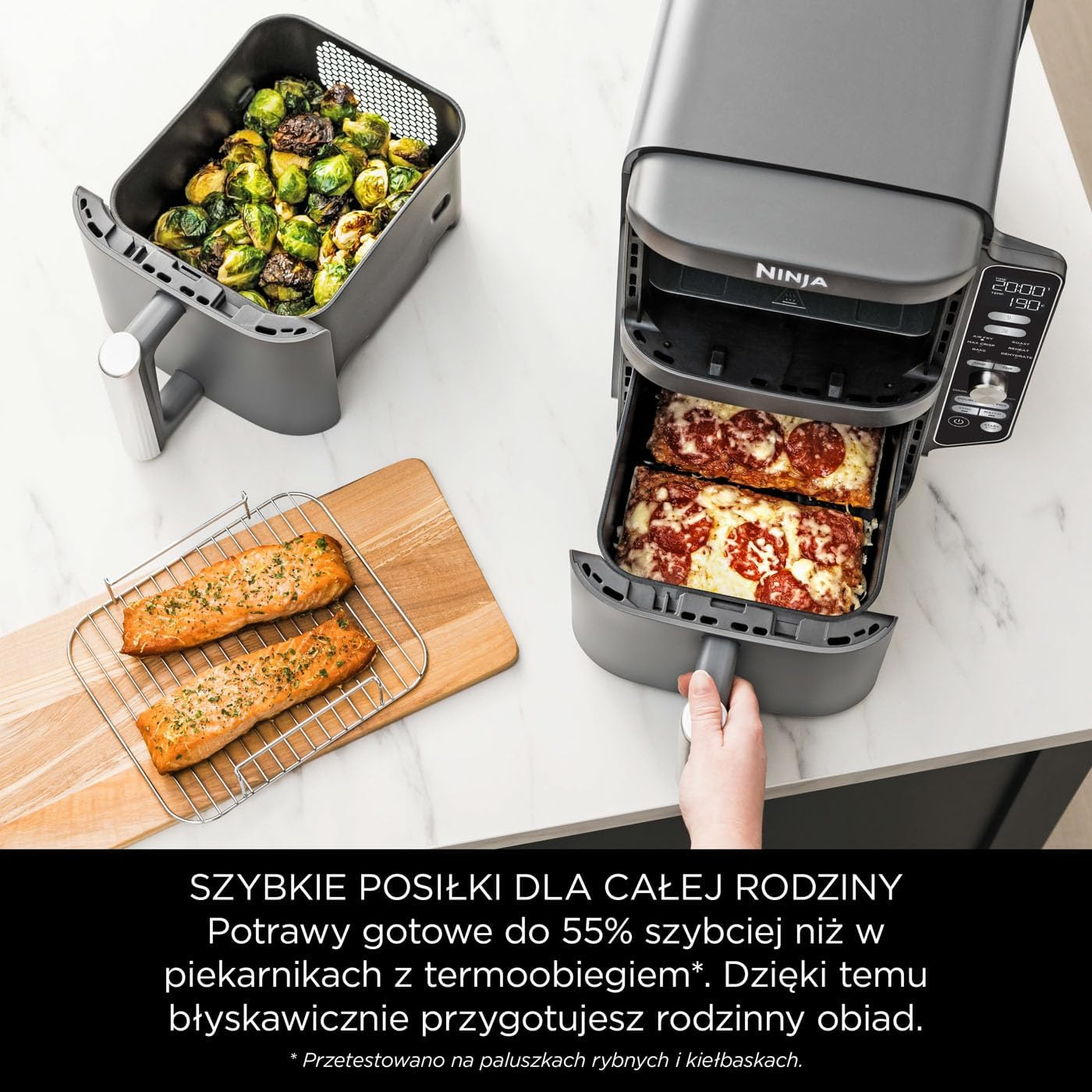 Frytownica beztłuszczowa z gotowym jedzeniem, w tym łososiem i pizzą, na białym blacie.