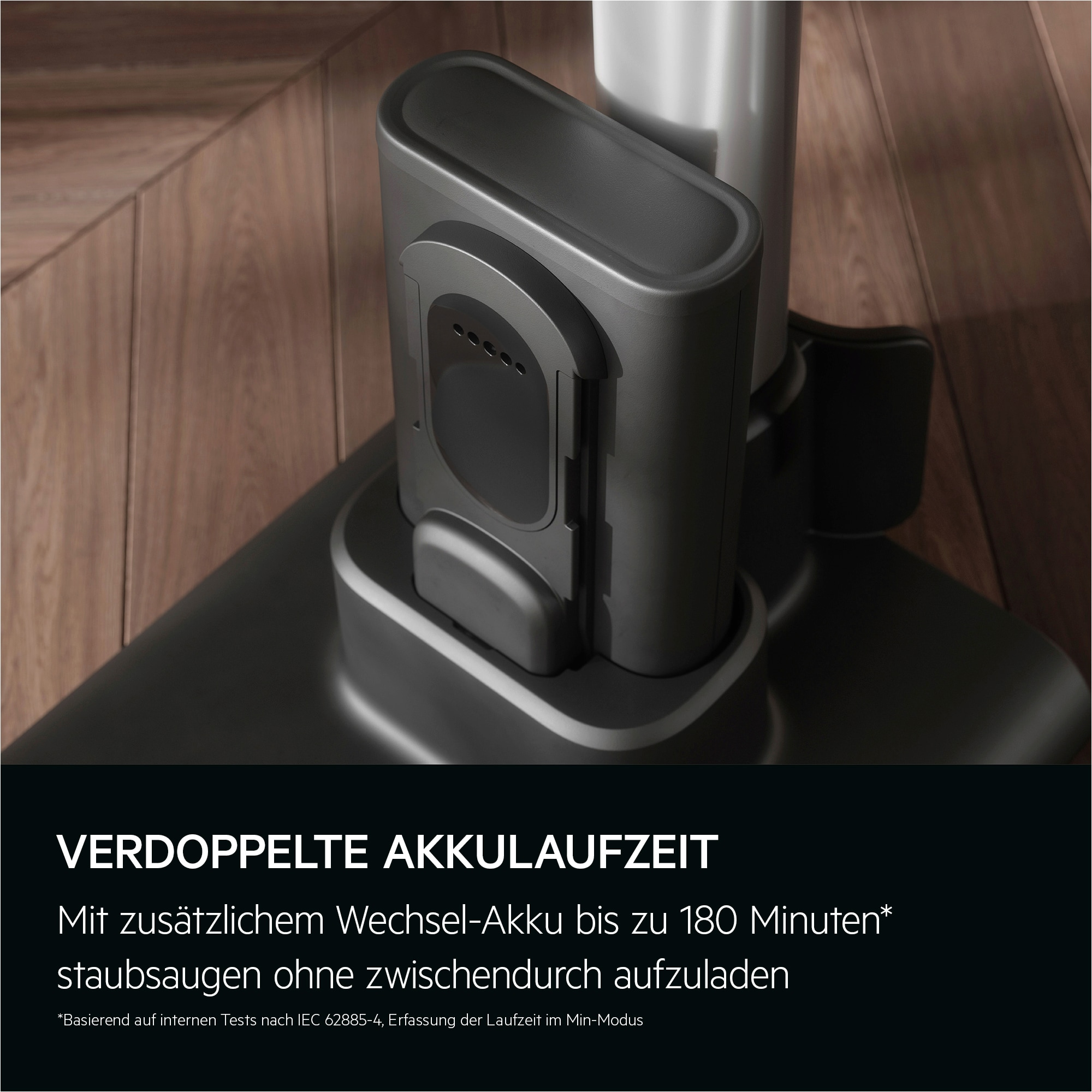 Ein dunkelgrauer Staubsauger-Akkupack. Er steht auf einer schwarzen Basis, im Hintergrund ein Holzboden.