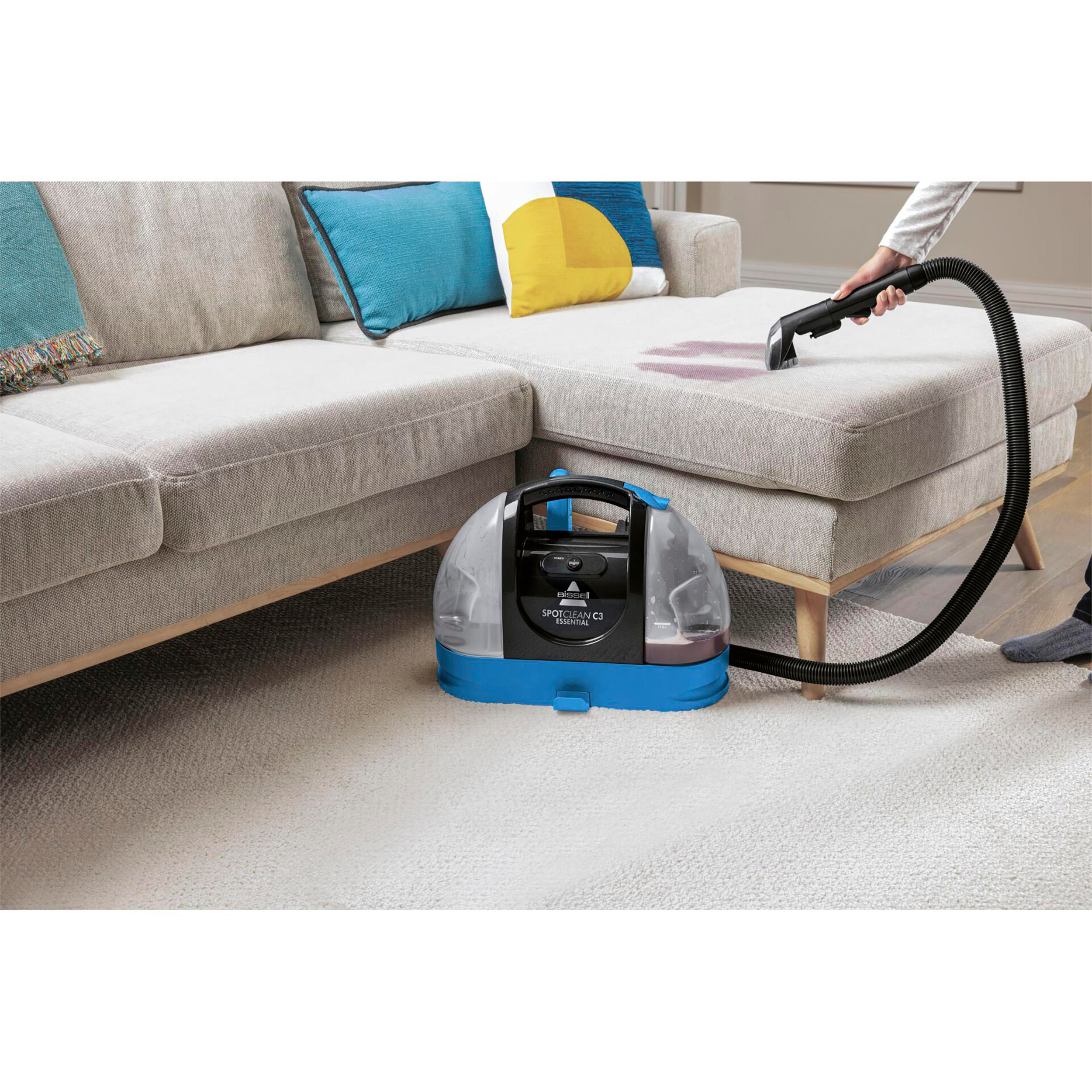 Eine Person verwendet einen Bissell SpotClean C3, um einen Fleck auf einem grauen Sofa zu reinigen.