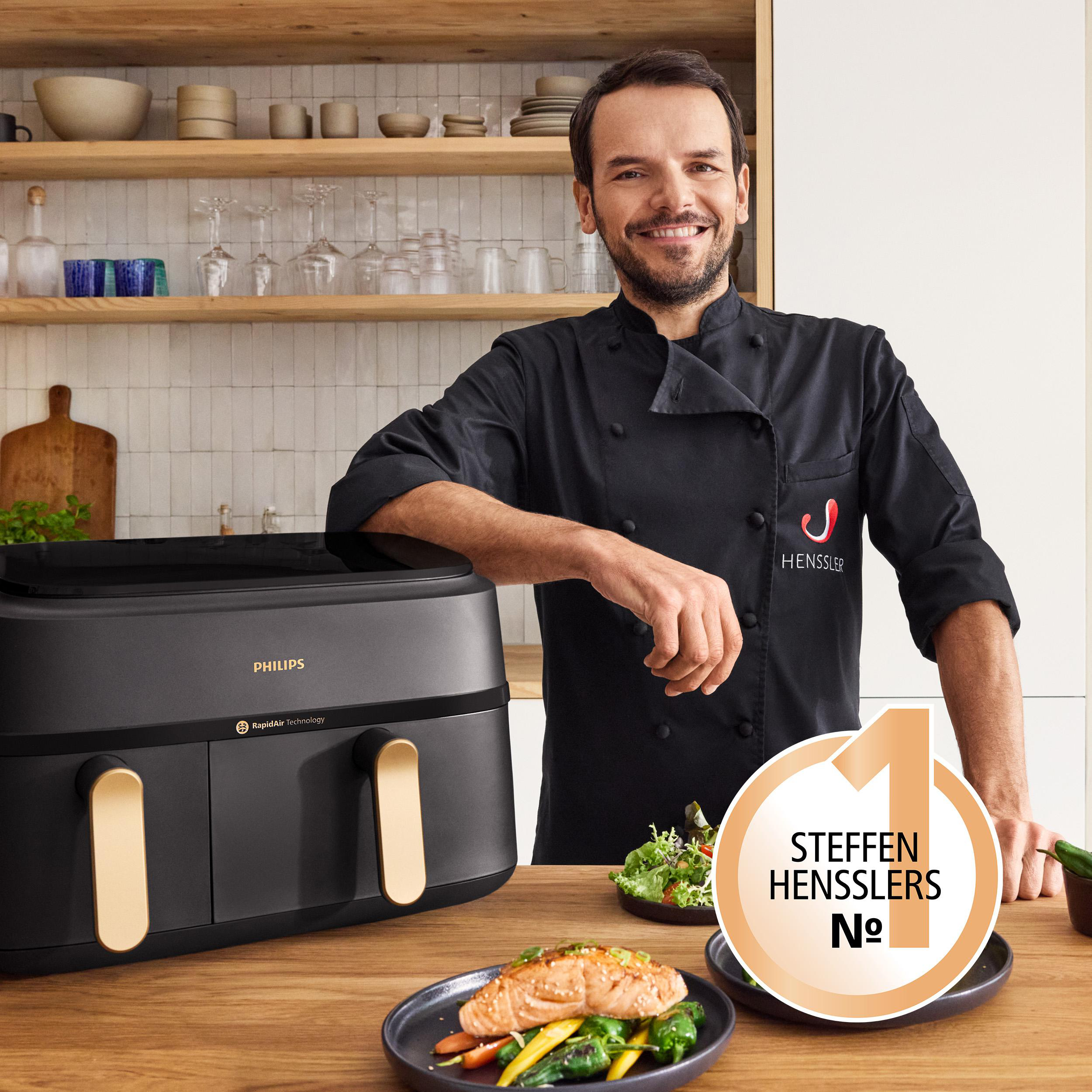 Koch mit Heißluftfritteuse und Essen. Die Friteuse ist schwarz und hat RapidAir.