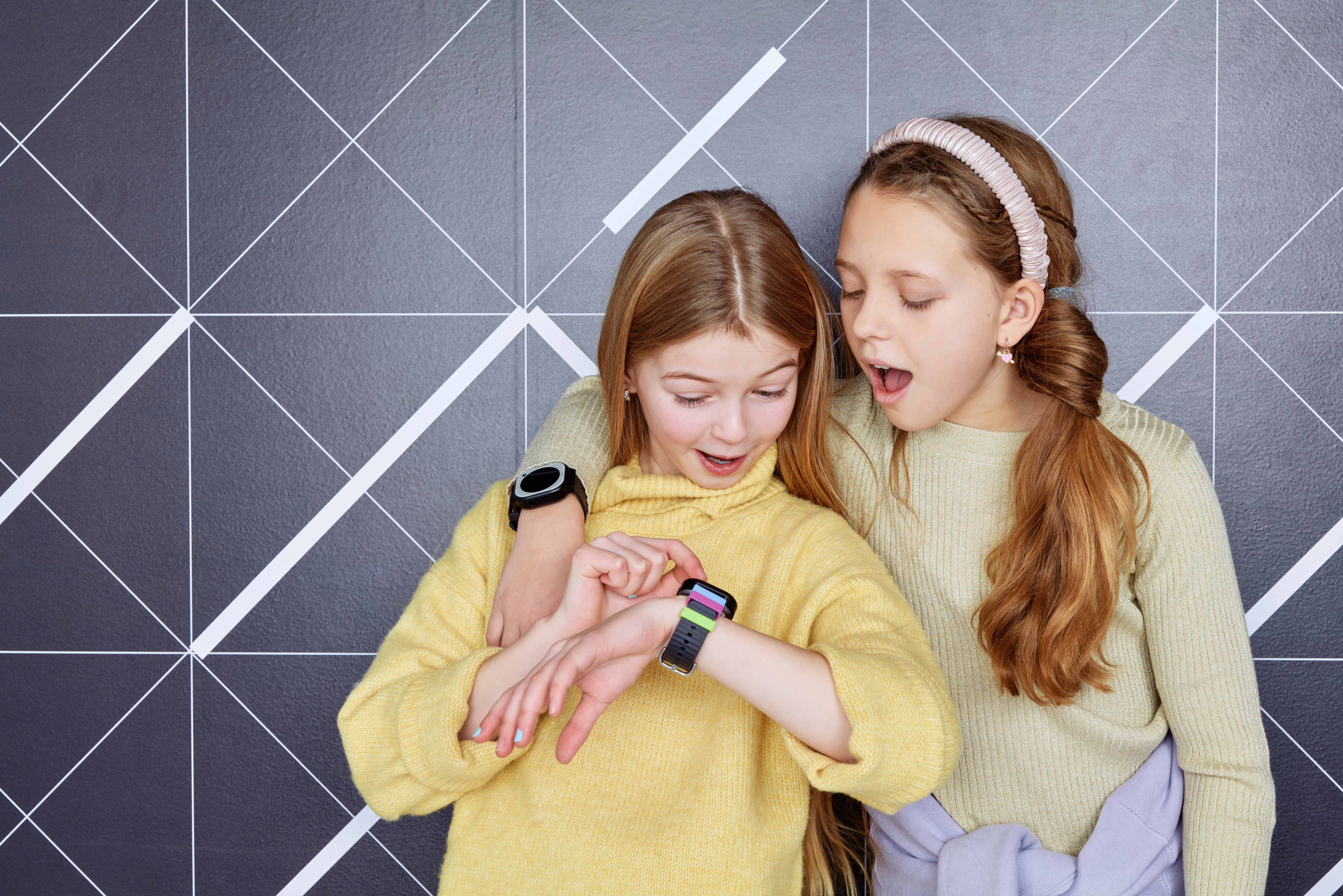 Zwei junge Mädchen schauen auf Smartwatches, eines ist überrascht.