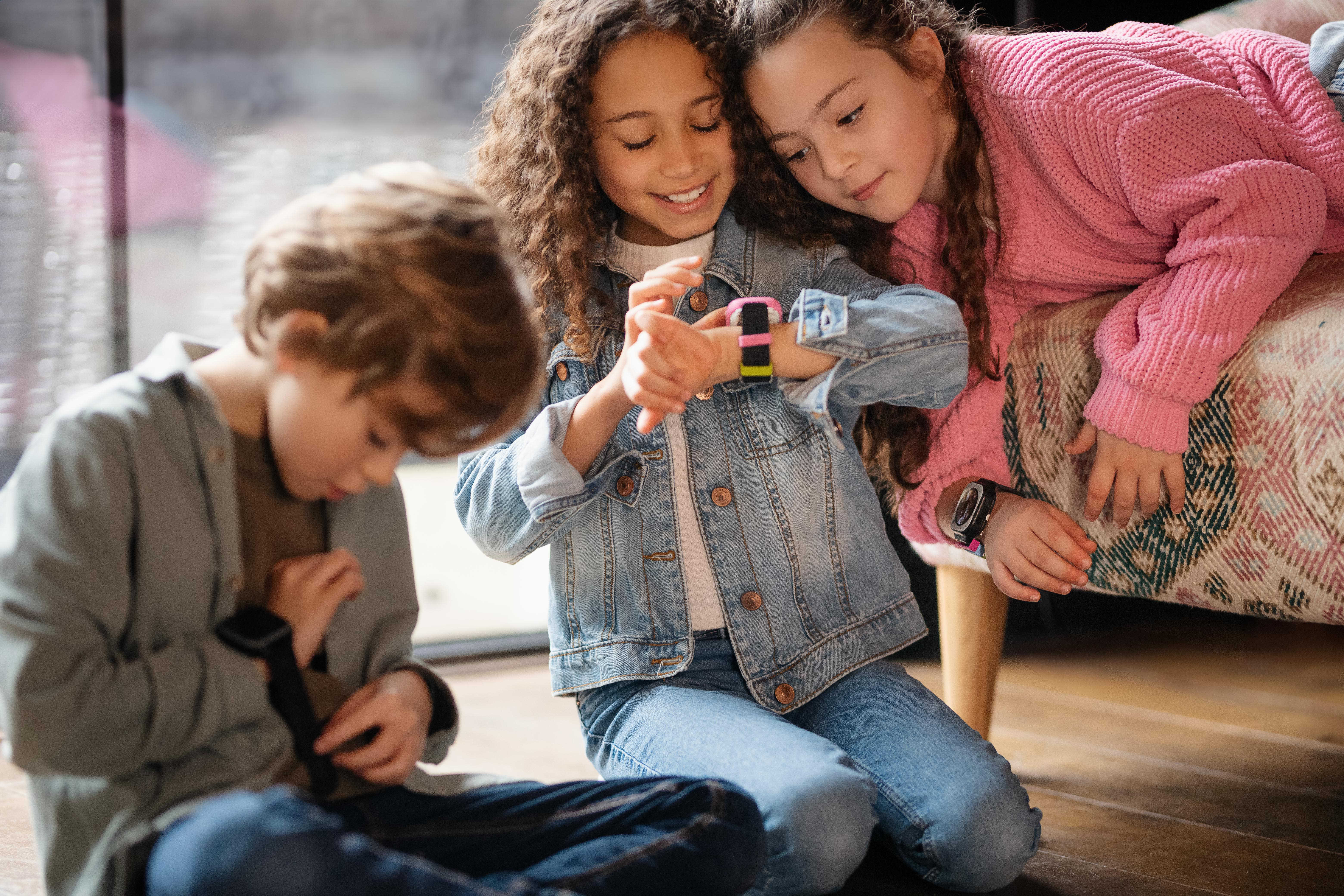 Drei Kinder betrachten eine Smartwatch am Handgelenk eines Mädchens, drinnen.