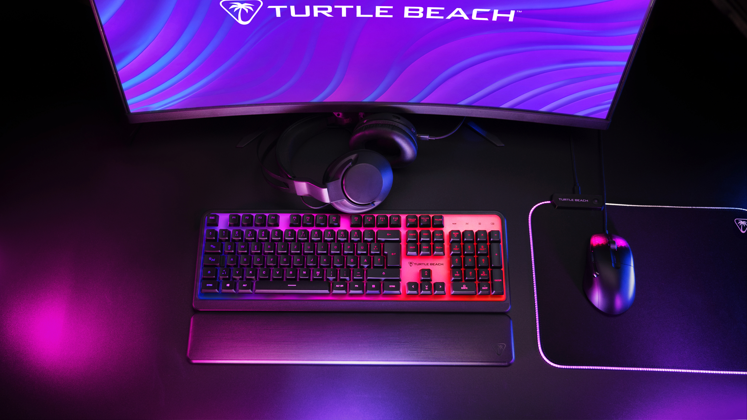 Gaming-Setup mit Tastatur, Maus, Kopfhörern und Monitor. Lila und rosa Umgebungsbeleuchtung.