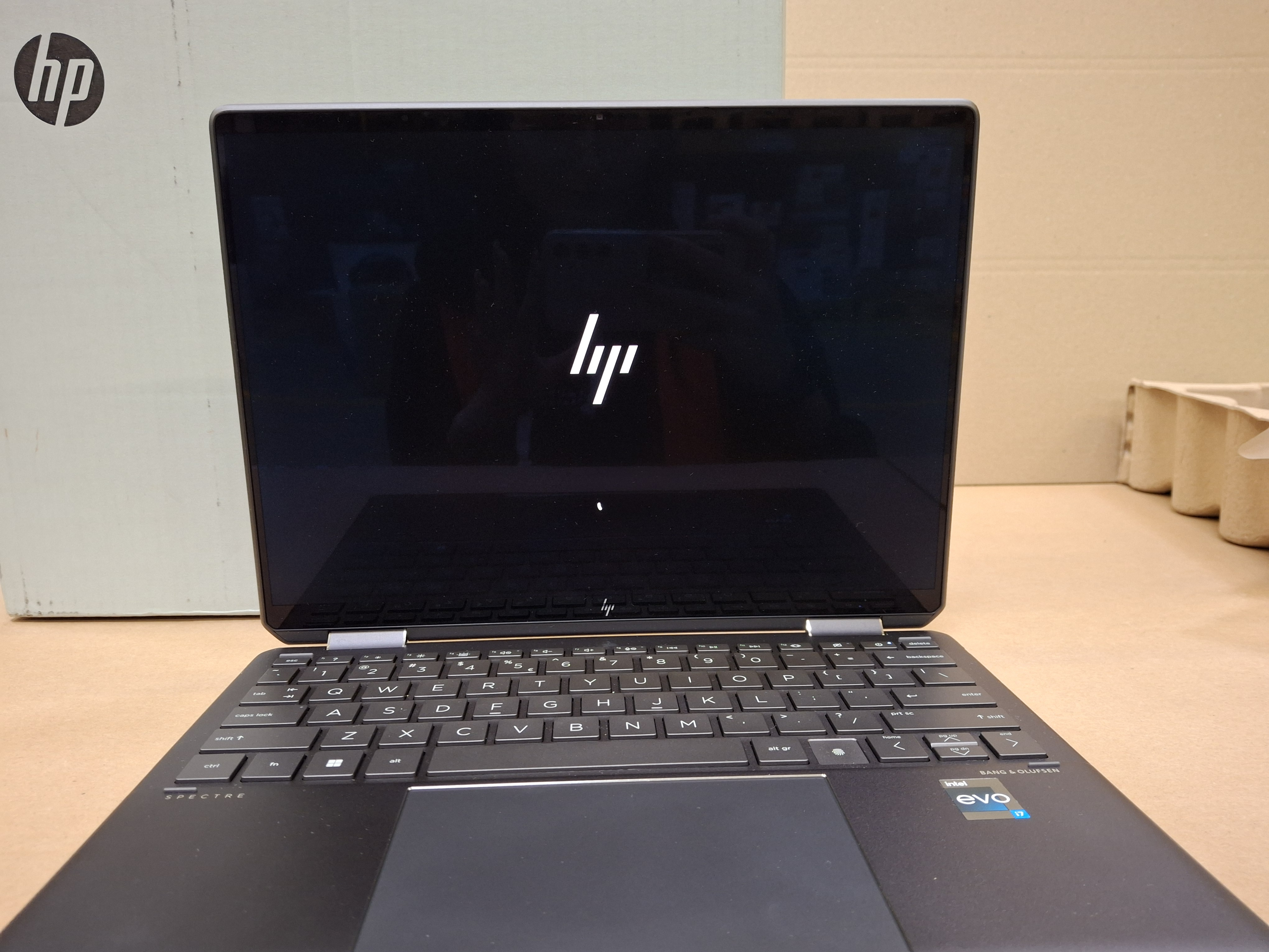 Laptop HP z białym logo na czarnym ekranie, otwarty na biurku.