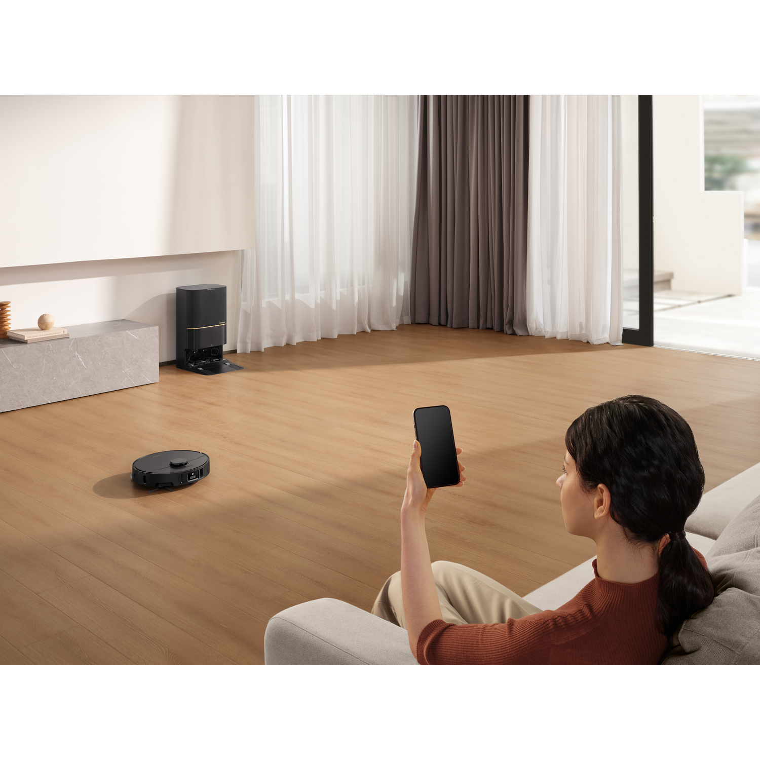 Vrouw op bank met telefoon, robot stofzuigen. Modern interieur.