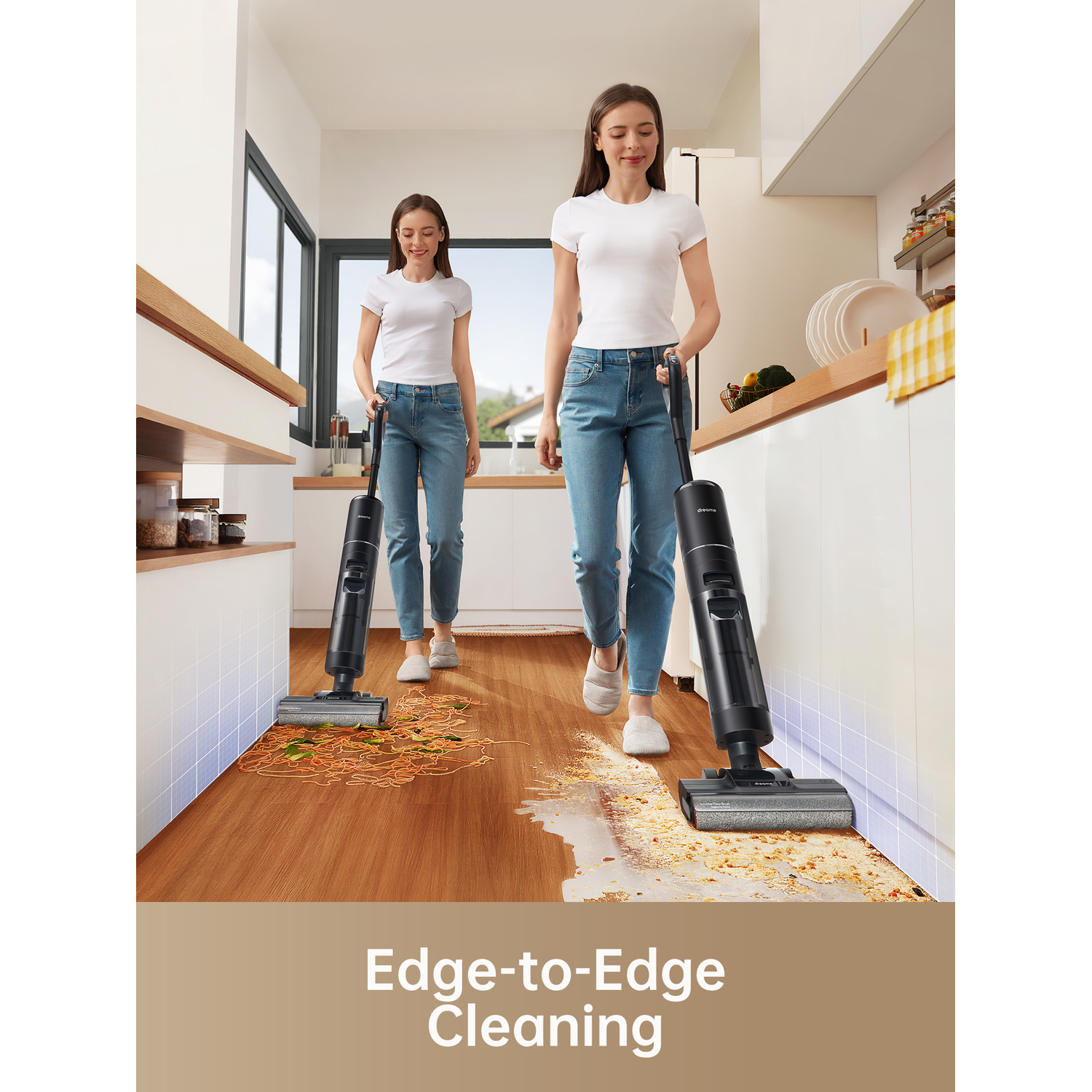 Two women in a kitchen cleaning with black and gray vacuum cleaners.