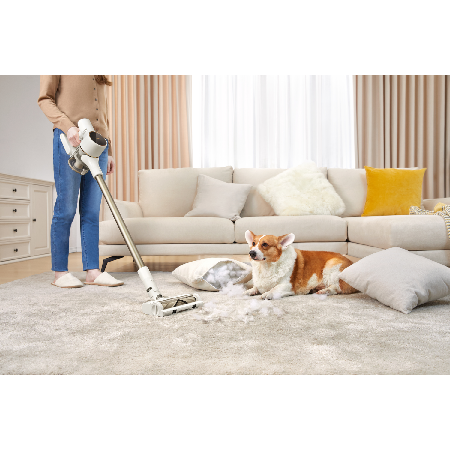 A person vacuuming a rug, a dog is resting on the rug, with a sofa in the background.