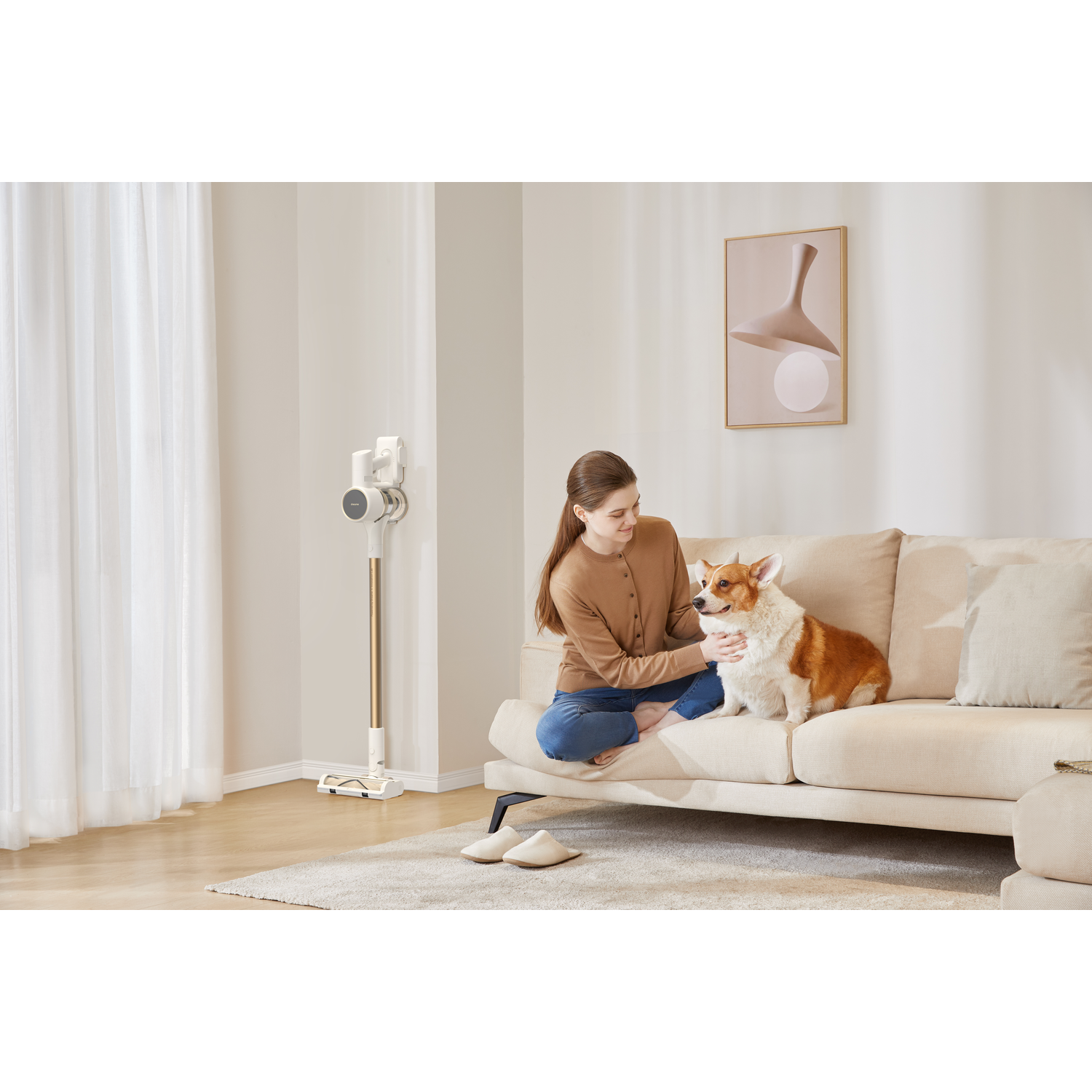 A woman on a sofa is petting a corgi, a vacuum cleaner is in the background.