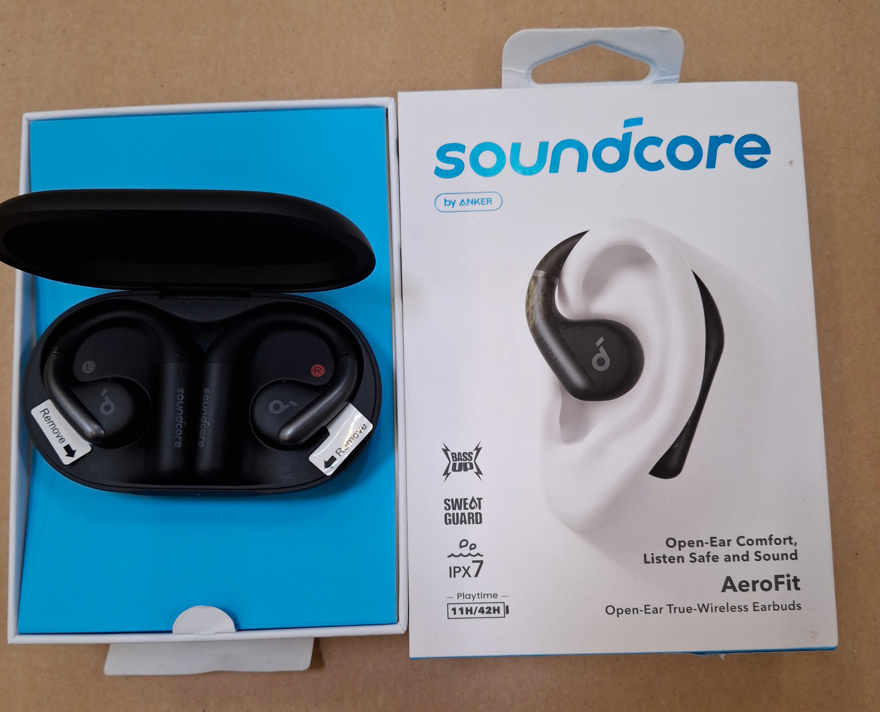 Słuchawki douszne w etui ładującym i pudełku. Na pudełku napis "soundcore" z obrazkiem ucha.