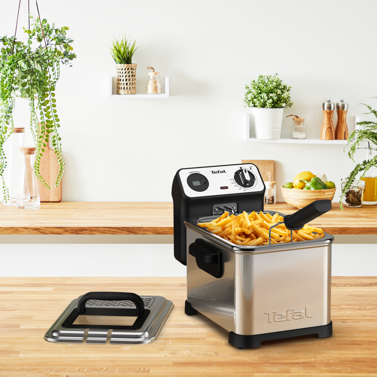 Tefal fritőz fa pulton. Sült krumpli belül, fedél és növények a háttérben.