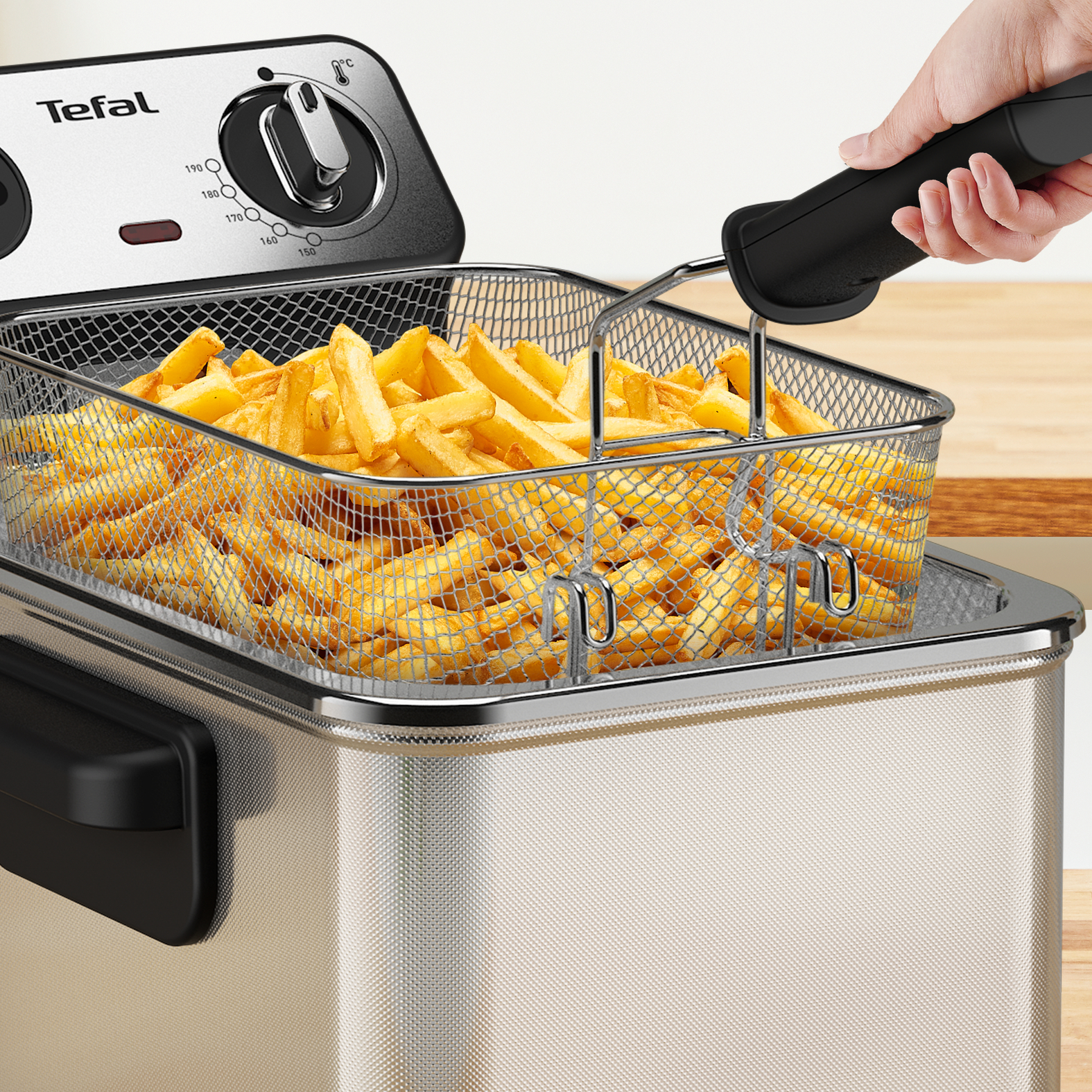 Sült krumplival teli sütőkosár kiemelése a fritőzből. Fa felület.