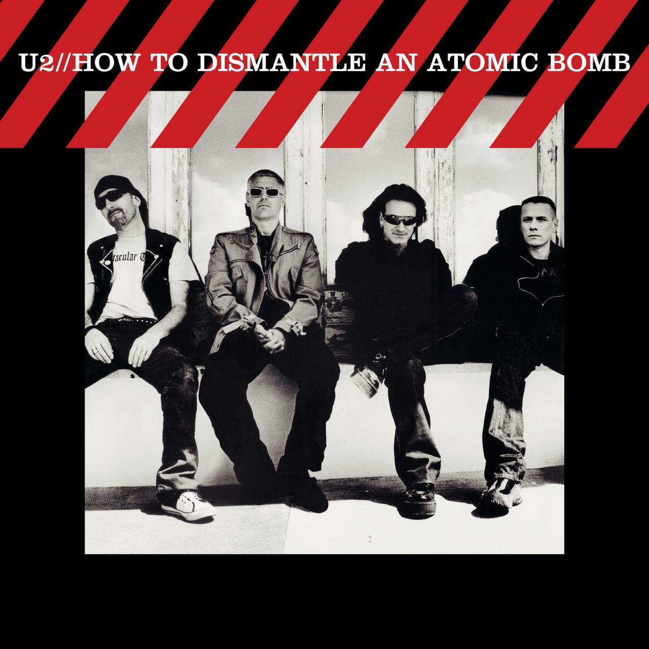 U2 albumhoes: U2 bandleden zitten. Rode en witte strepen bovenaan.