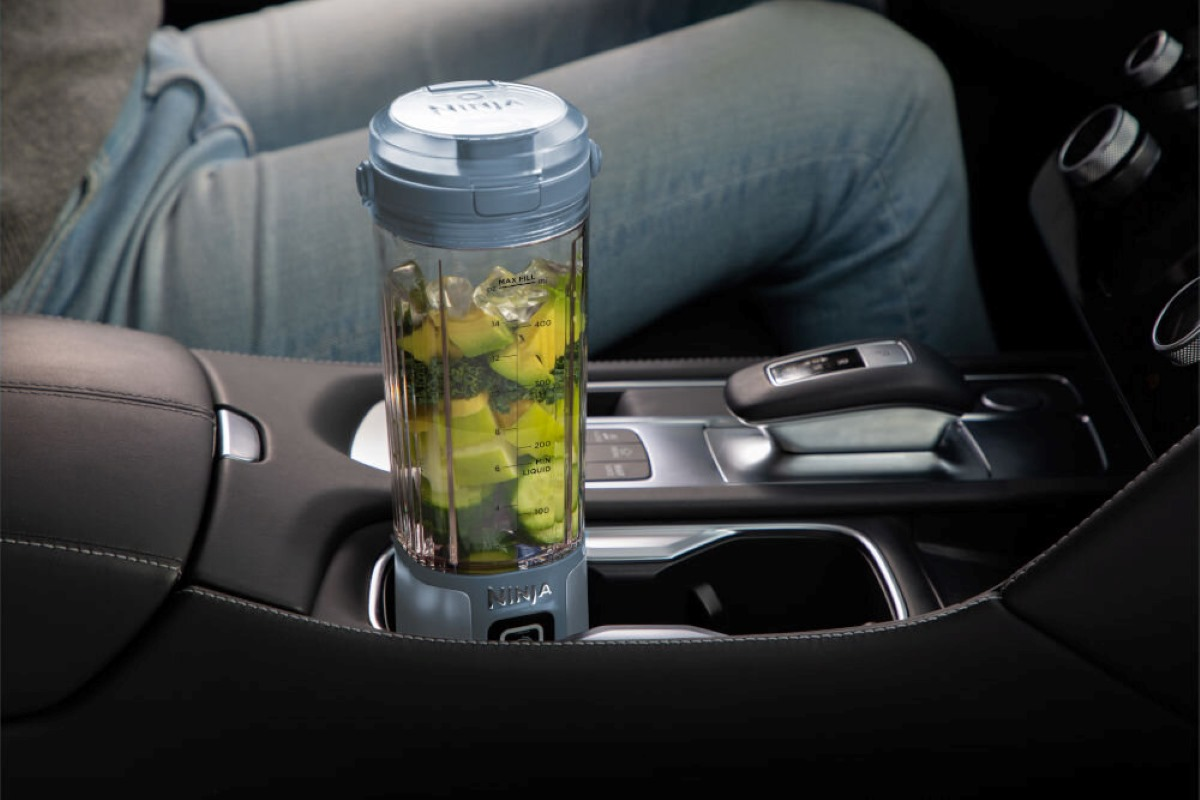 Blender w uchwycie na kubek w samochodzie ze smoothie. Osoba siedzi w samochodzie.
