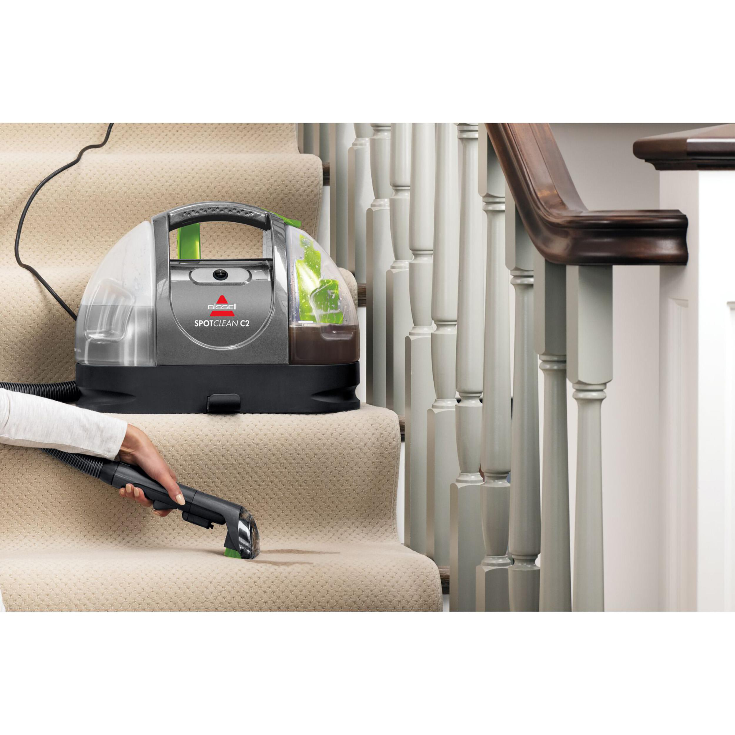 Eine Person reinigt Treppen mit einem Bissell SpotClean C2, saugt einen Teppich.