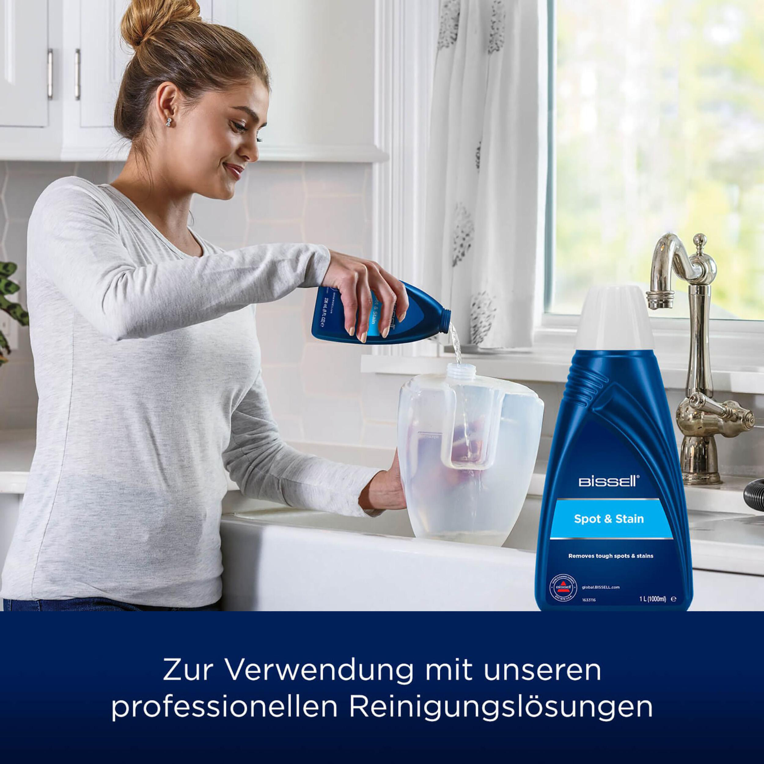 Frau gießt Bissell Spot & Stain Reiniger in einen Wassertank am Küchenbecken, Flasche im Bild.