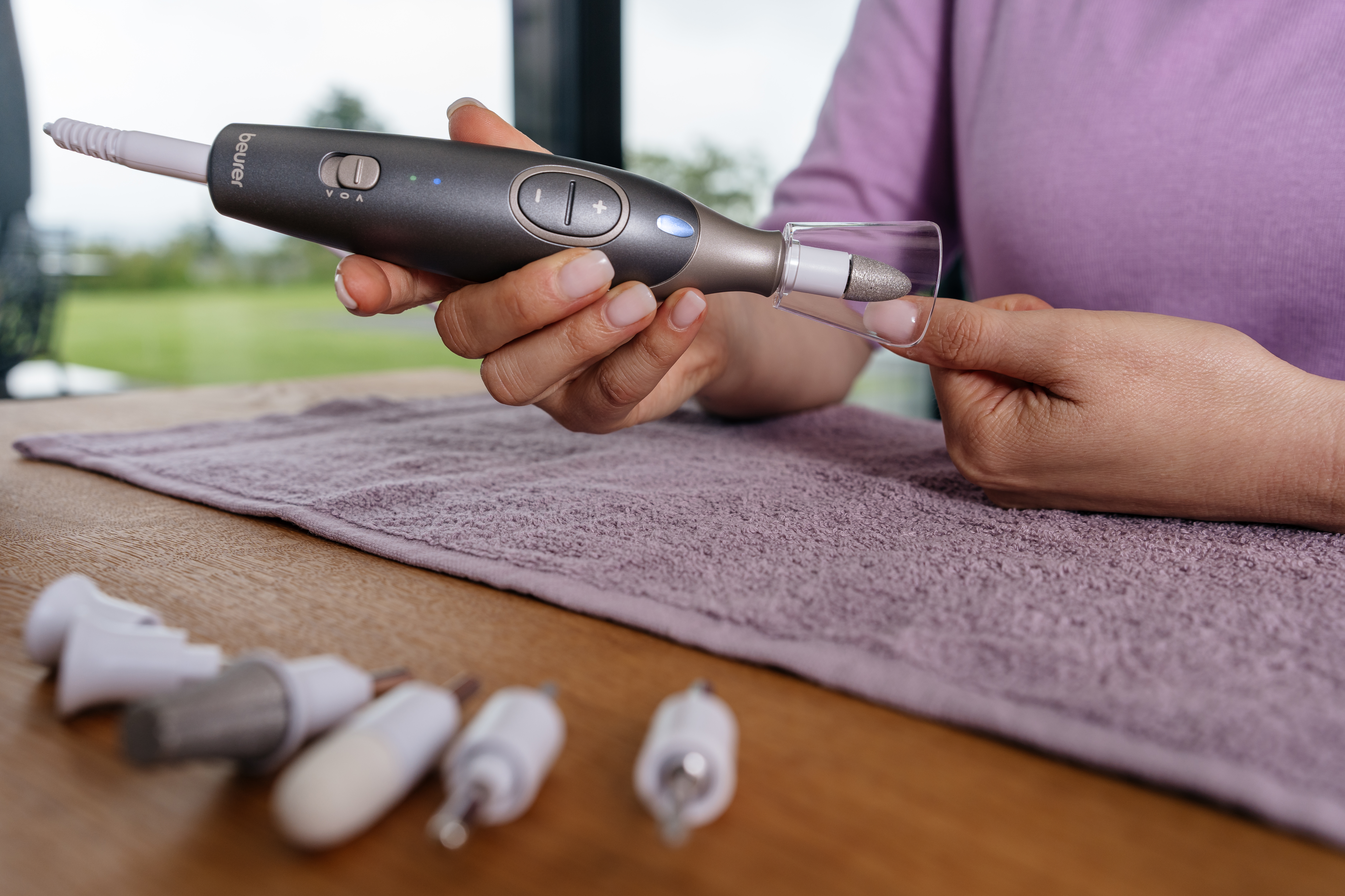 Une personne utilise un outil de soin des ongles. L'outil est tenu près d'un doigt. Plusieurs accessoires sont sur la table.
