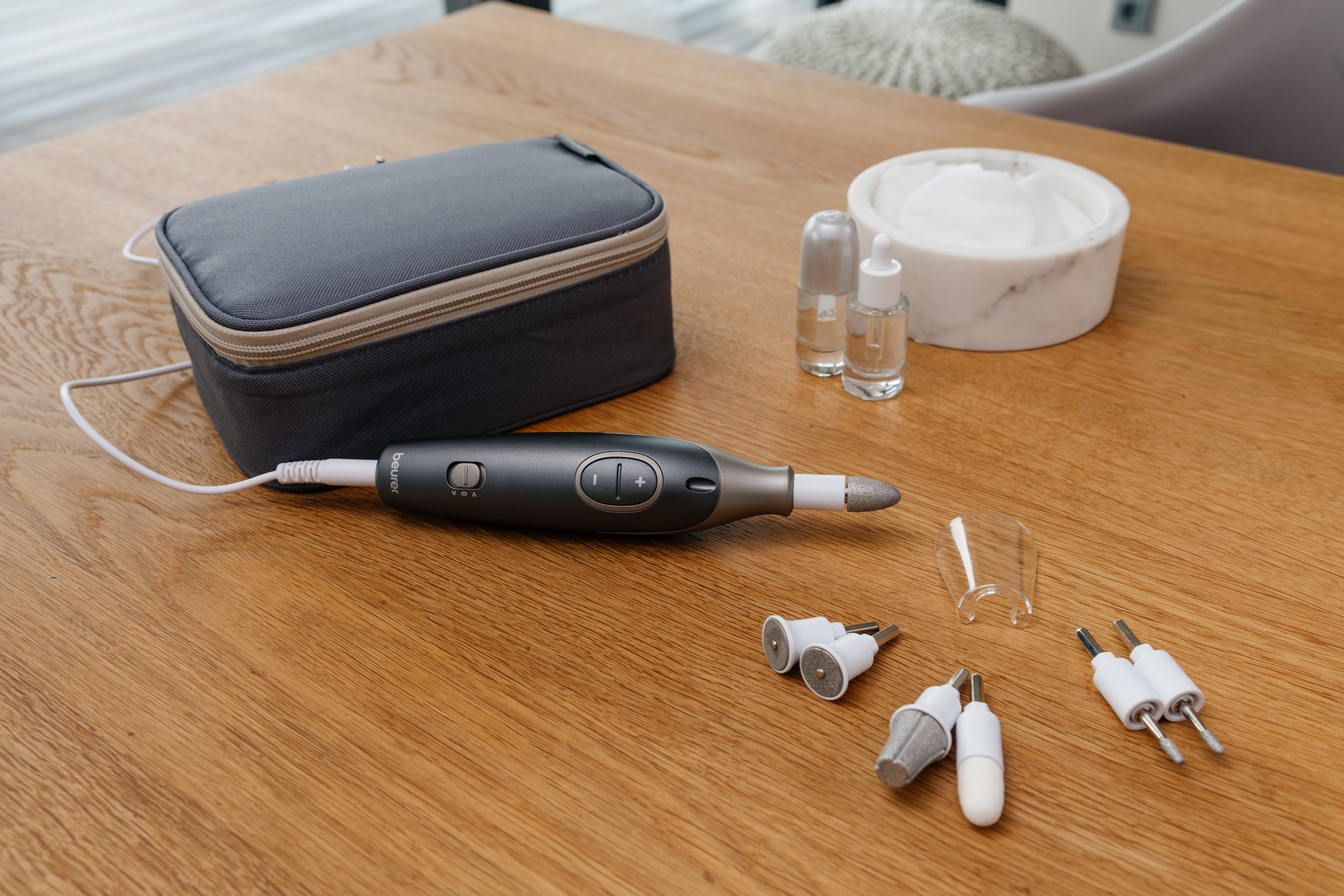 Set de soin des ongles sur table en bois. Comprend une trousse grise, une perceuse à ongles, des flacons.