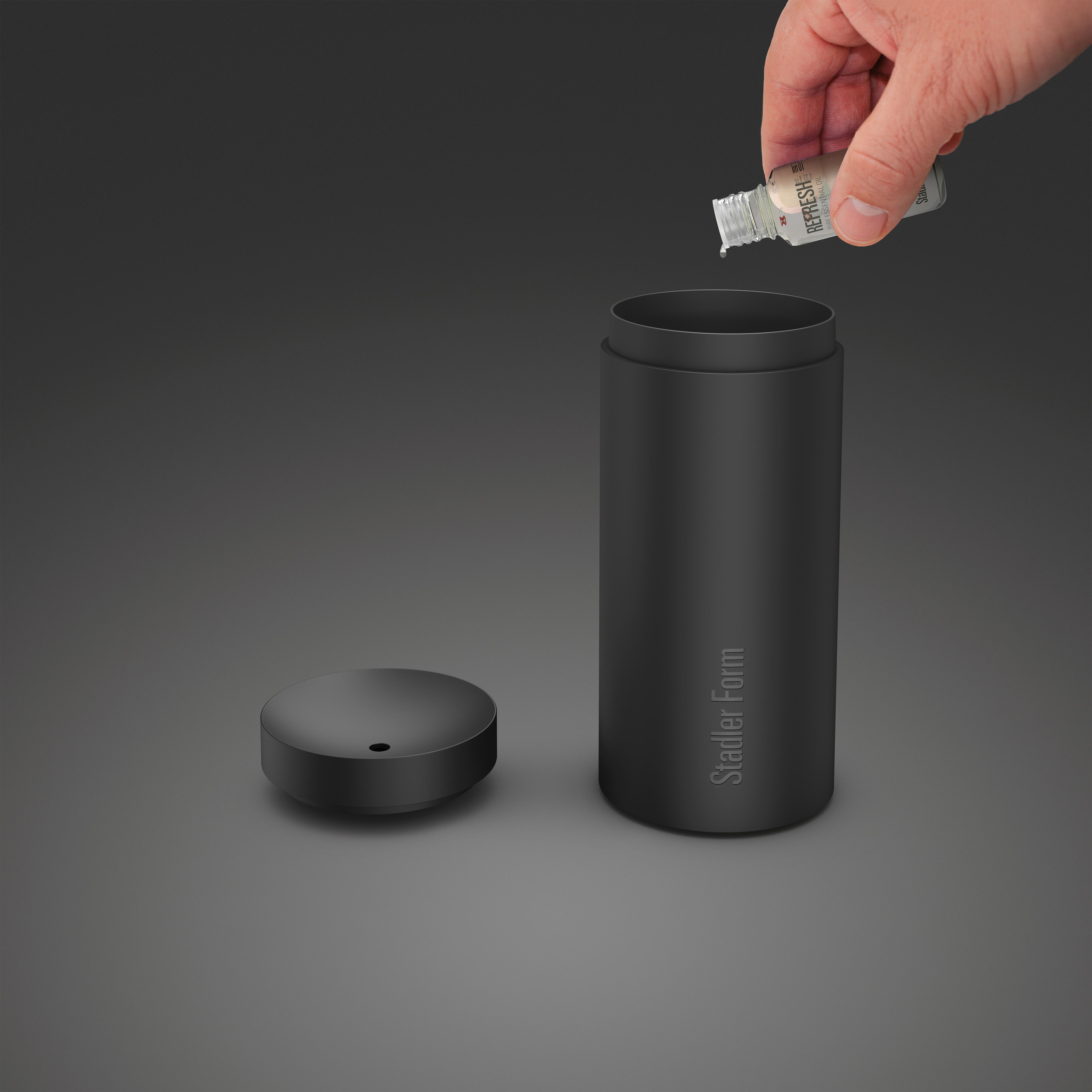 Eine Hand gießt eine Flüssigkeit aus einer kleinen Flasche in einen schwarzen Behälter.