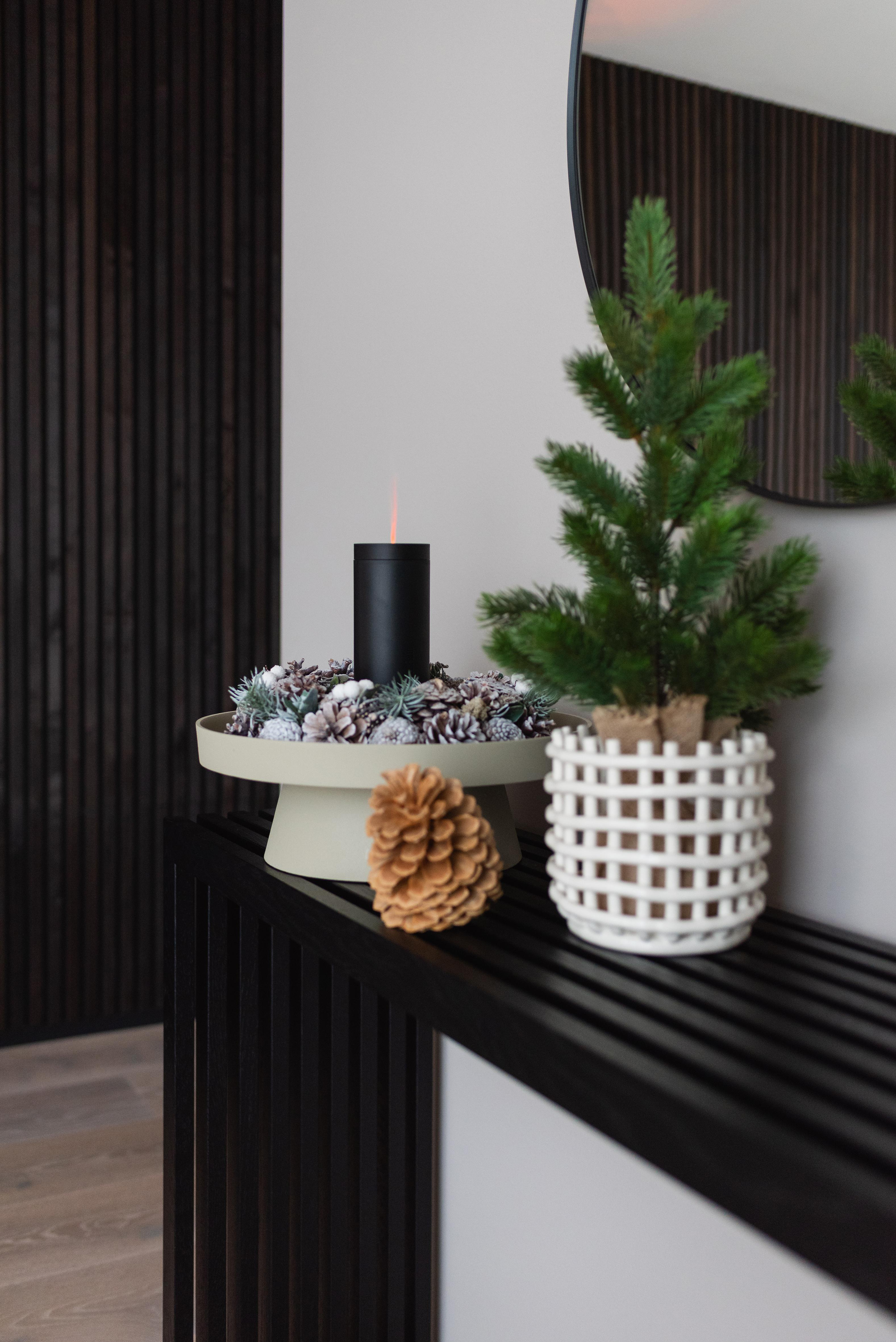 Ein Tisch mit einer schwarzen Kerze auf einem Ständer mit Dekorationen. Ein Weihnachtsbaum und ein Spiegel im Hintergrund.