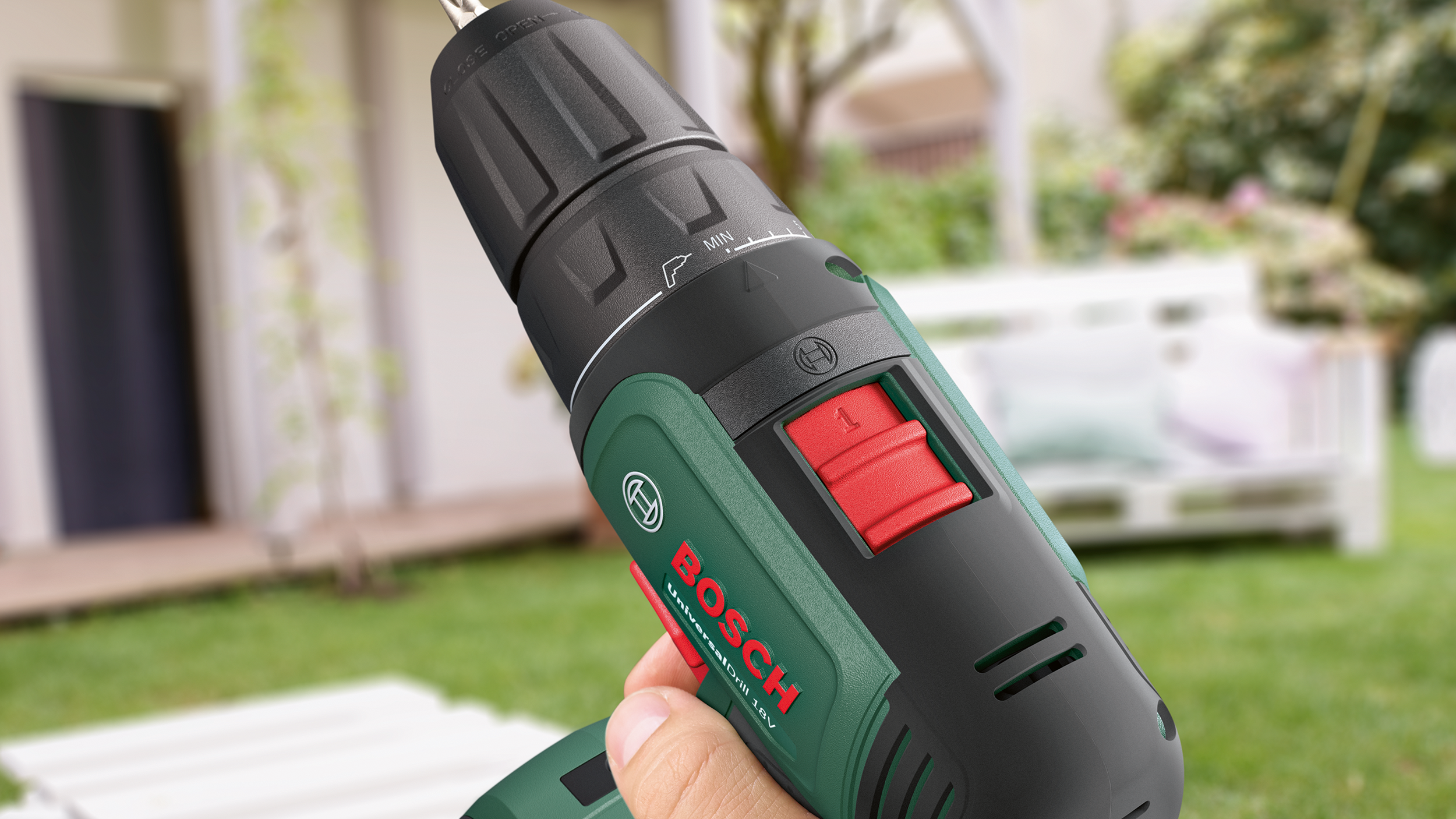Bosch fúró: Egy kéz egy zöld-fekete Bosch fúrót tart, piros kapcsolóval.