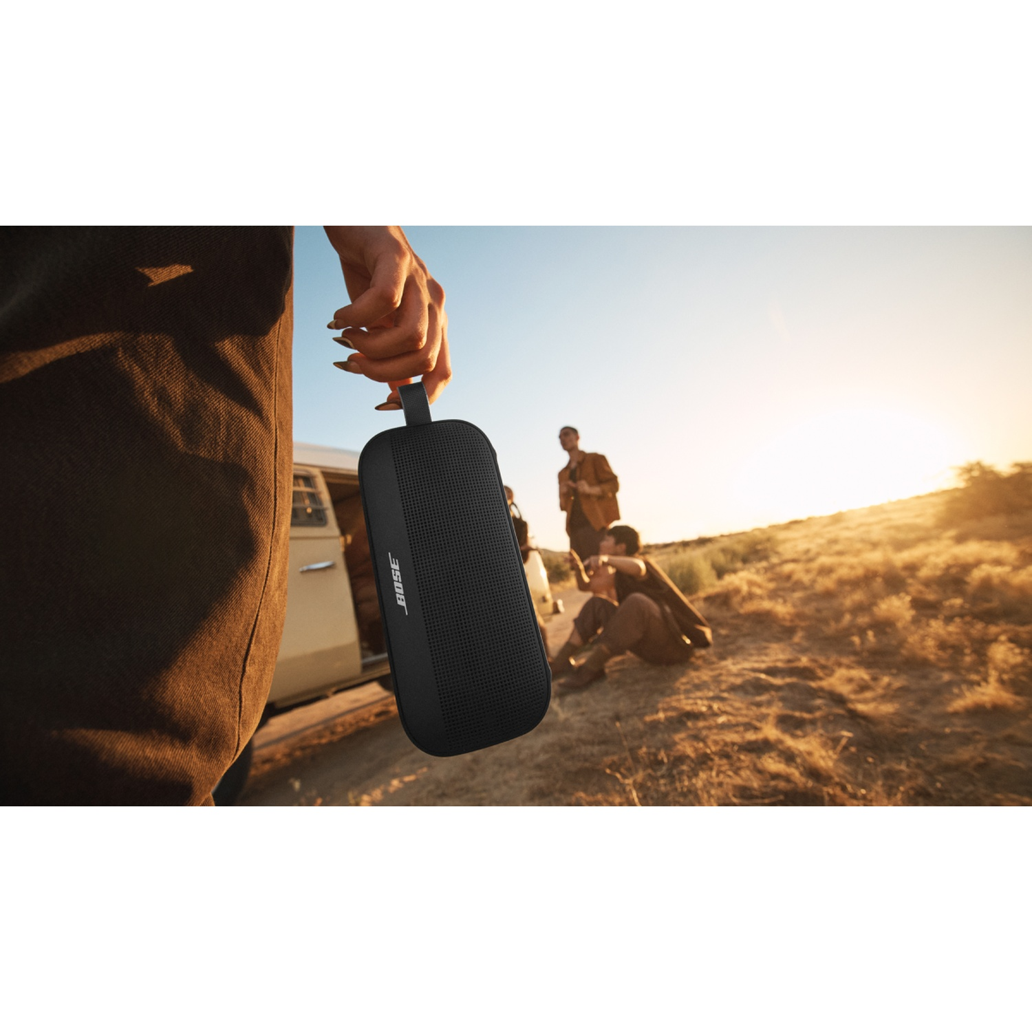 Una persona tiene in mano un altoparlante portatile nero vicino a persone sedute all'aperto.