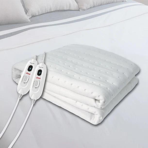 Manta eléctrica blanca en una cama. Dos controladores son visibles en el lado izquierdo.