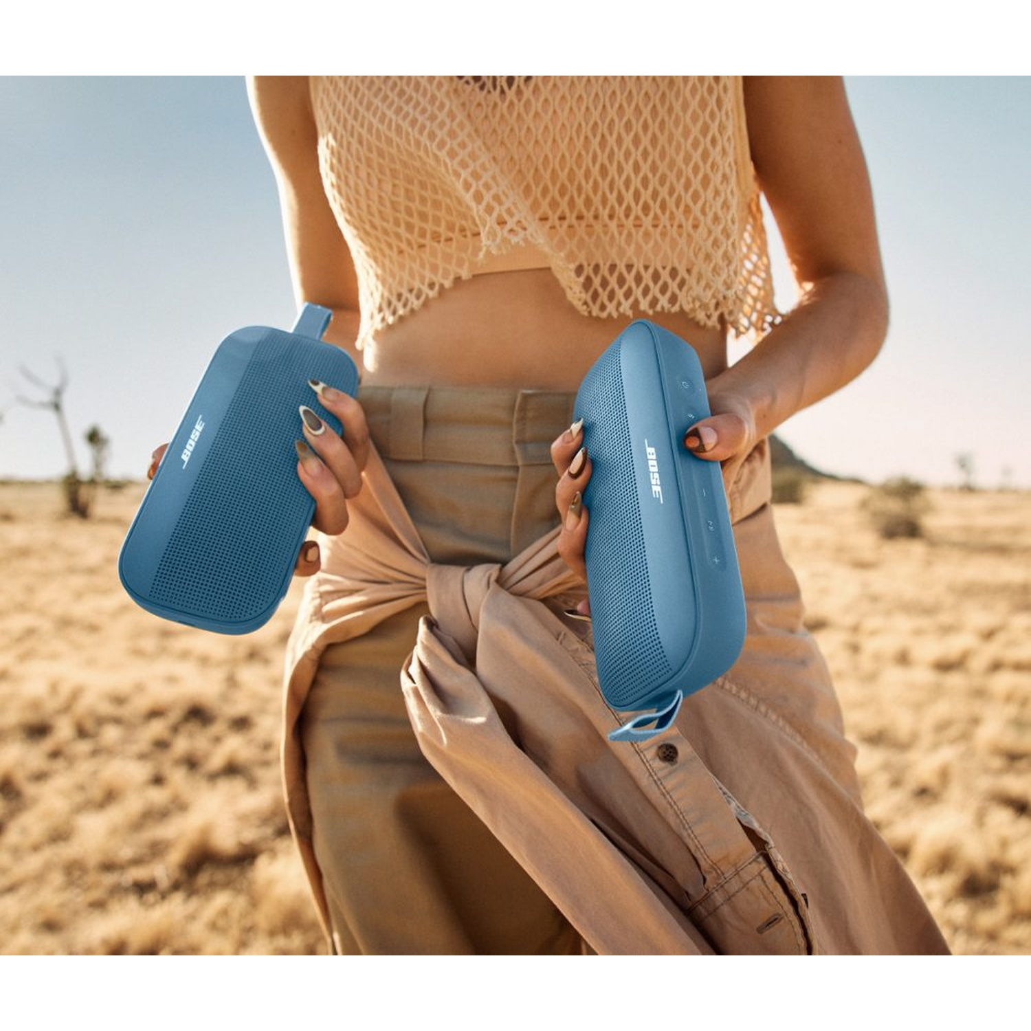 Due altoparlanti Bose blu tenuti da una donna in un ambiente desertico.