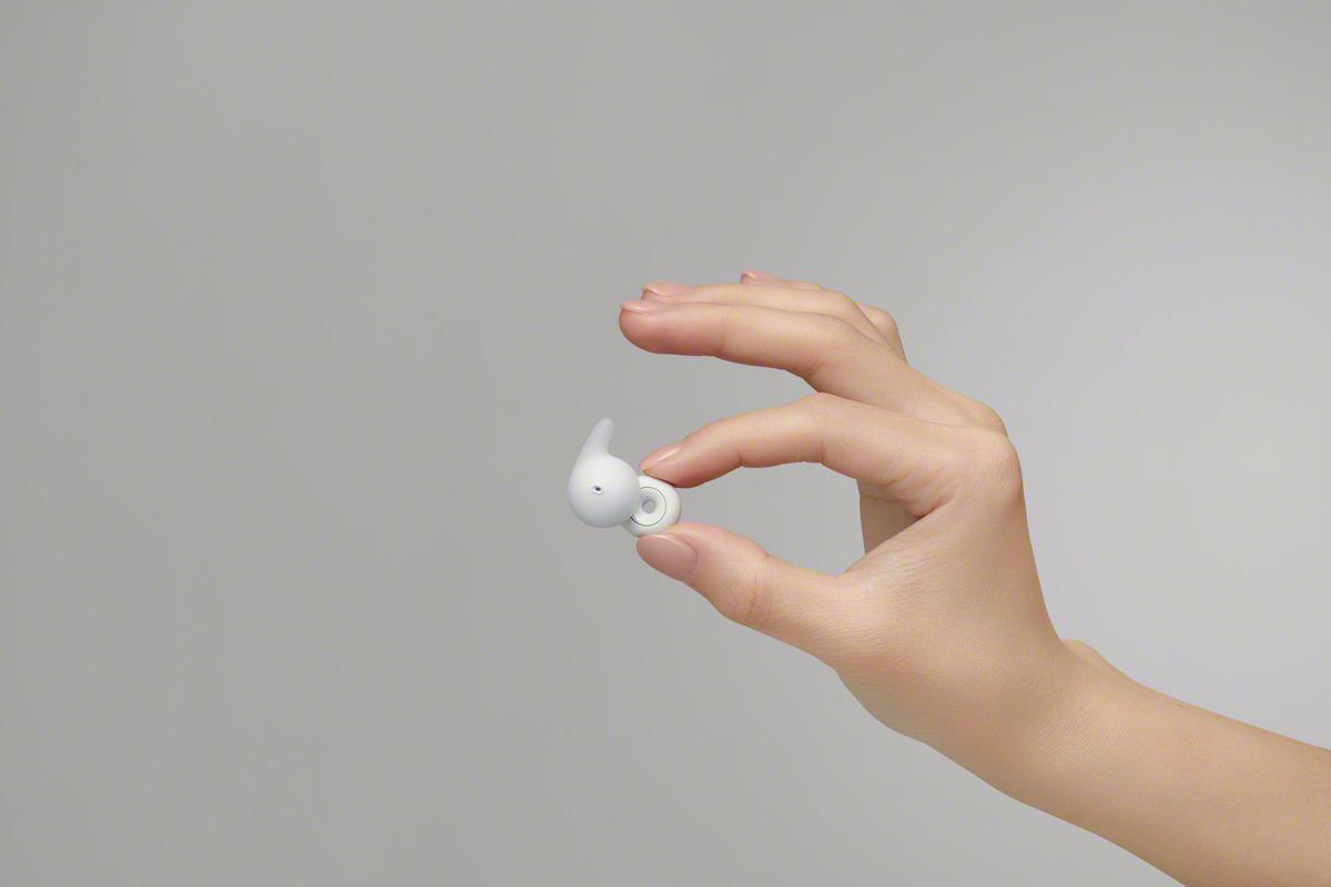 Eine Hand, die einen weißen Ohrhörer vor grauem Hintergrund hält.