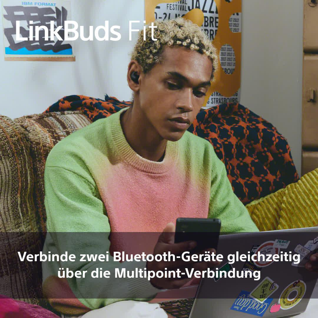 Ein junger Mann mit Ohrhörern, der auf ein Telefon und einen Laptop schaut.
