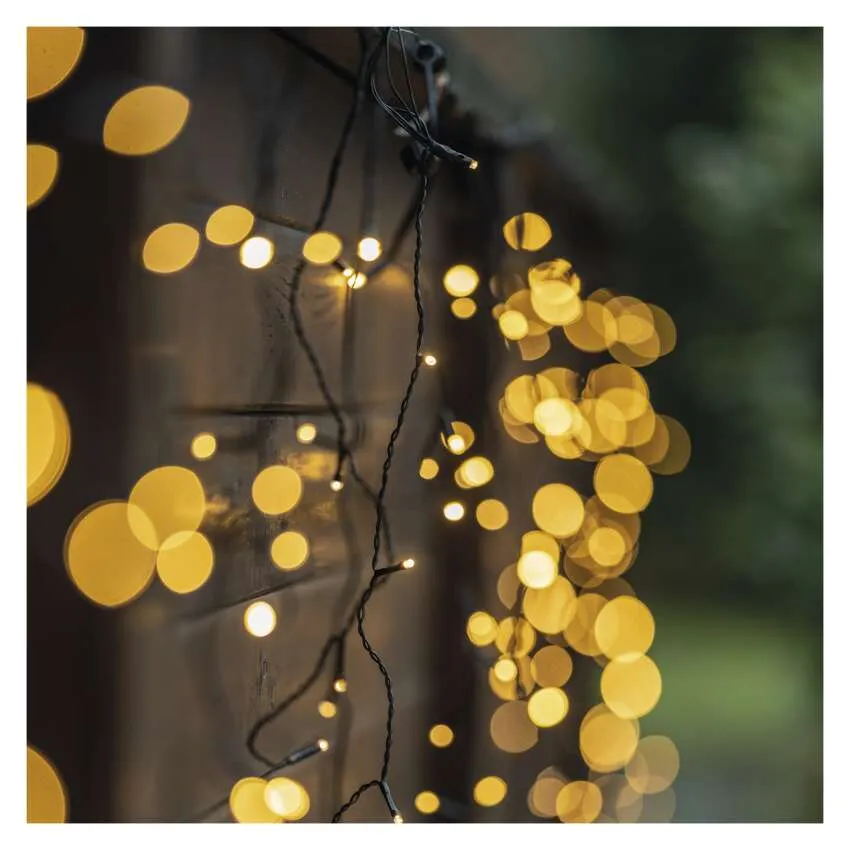 Füzérfények meleg sárga fényekkel egy fa kerítés előtt, bokeh effektusokat alkotva.