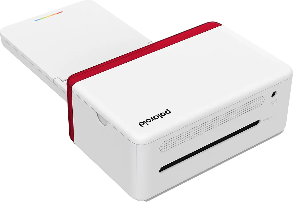 Fehér Polaroid nyomtató piros díszítéssel. Felső fedél nyitva, szivárvány csíkkal. Fekete nyílás a fotók számára elöl.