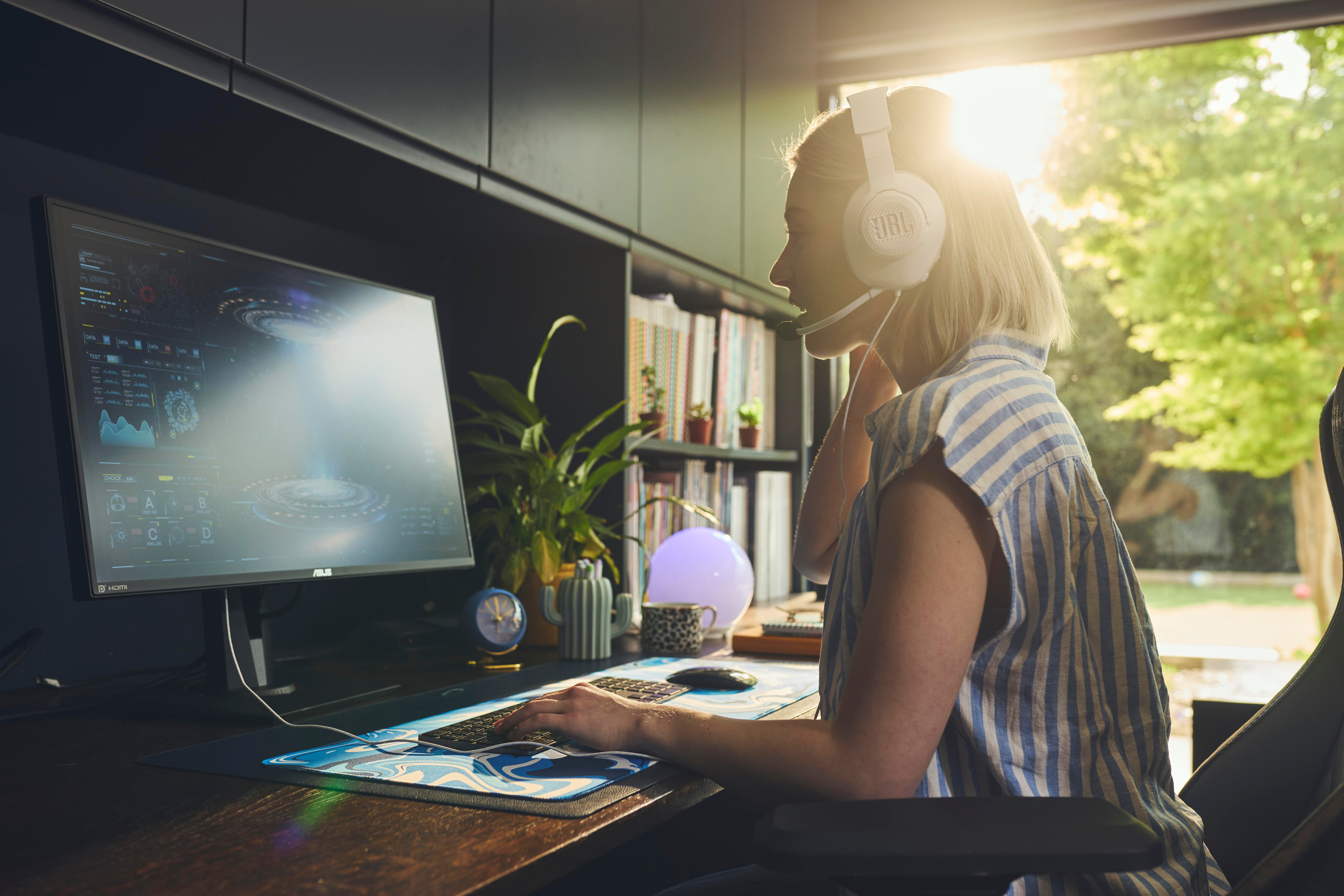 Eine Frau mit Kopfhörern spielt an einem Computer mit hellem Bildschirm.