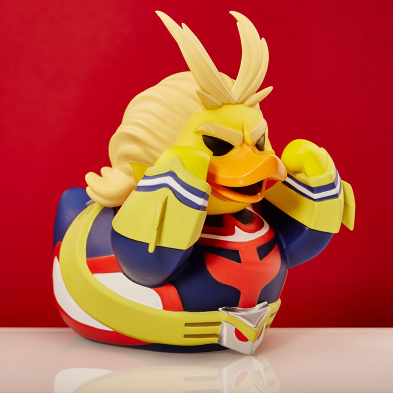 Egy sárga kacsa játék, amely a My Hero Academia All Might-jaként van öltözve, piros háttérrel.