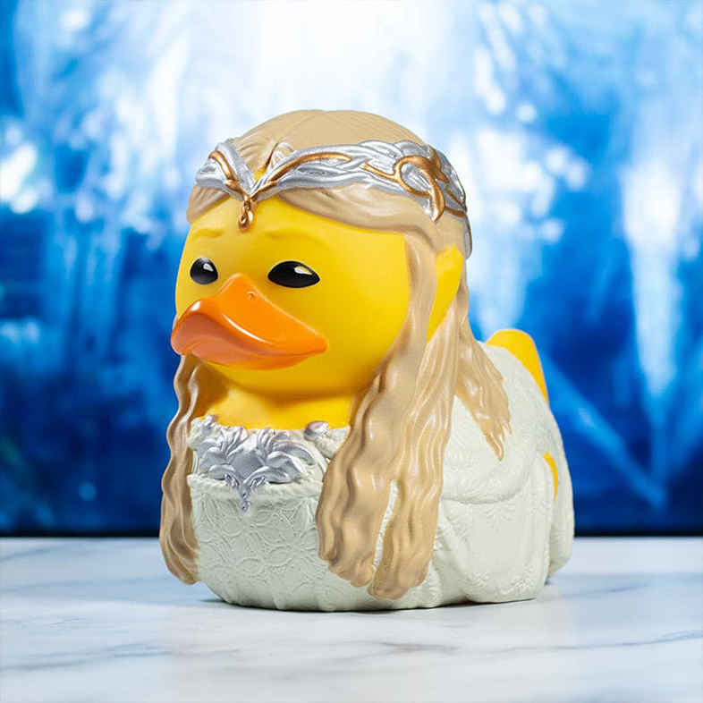 Sárga gumikacsa szőke hajjal, ezüst koronával és fehér ruhával, kék háttérrel.