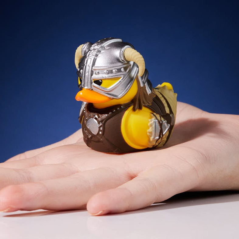 Gumikacsa viking sisakban, kézben tartva, kék háttér előtt.