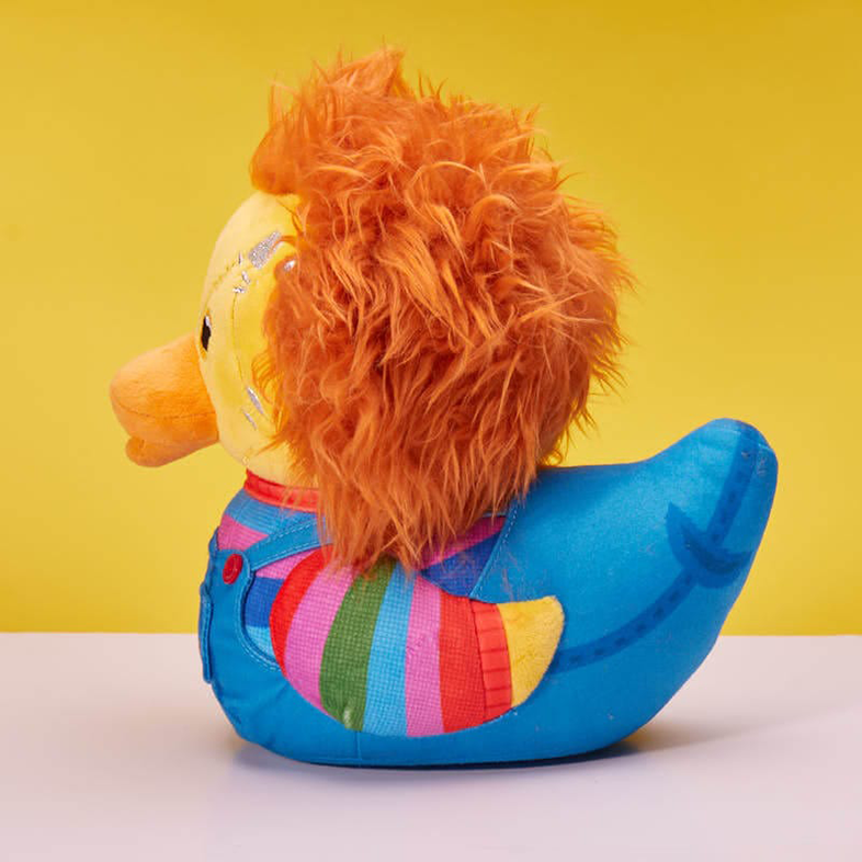Chucky baba kacsa játék narancssárga hajjal, sárga arccal, kék testtel csíkos inggel. Sárga háttér.