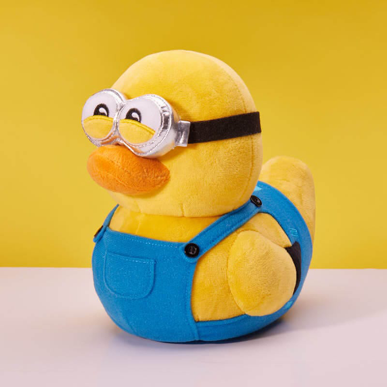 Minion béka játék szemüveggel, kék kezeslábassal és sárga testtel. Sárga háttér.
