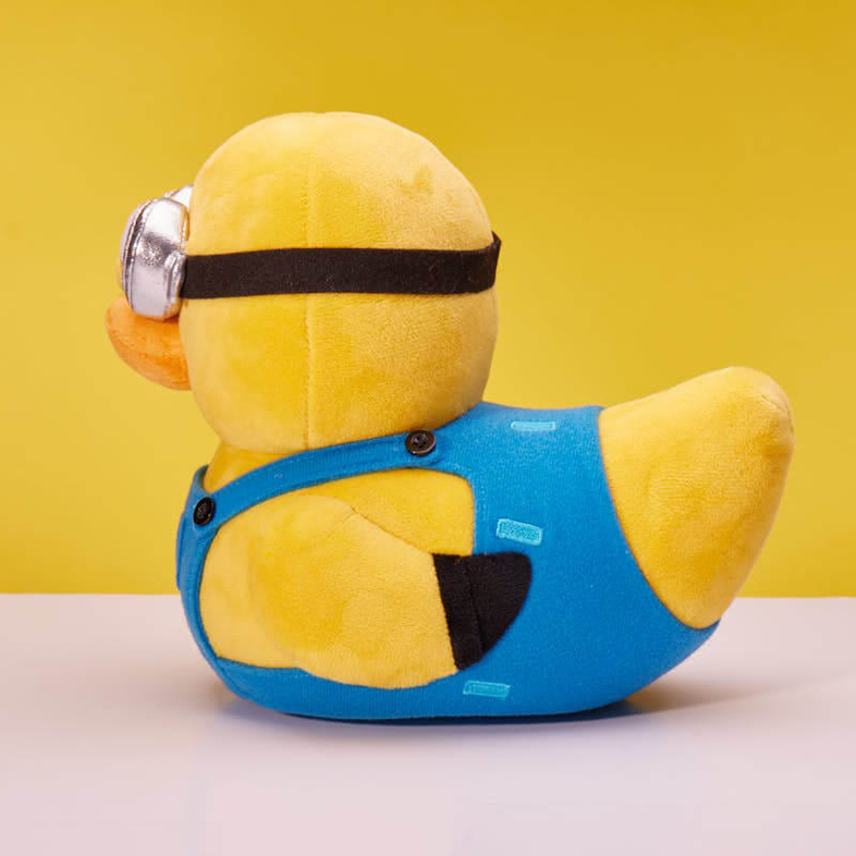 Egy sárga Minion kacsa játék, szemüveggel és kék kezeslábassal, sárga háttérrel.