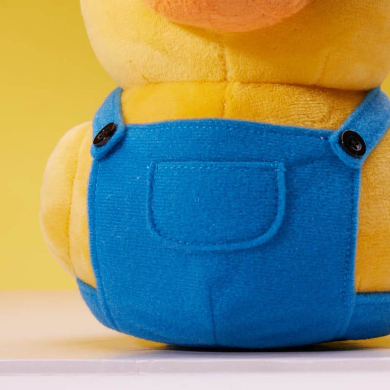 Közelkép egy Minion béka játékról, kék kezeslábassal és sárga testtel. Sárga háttér.